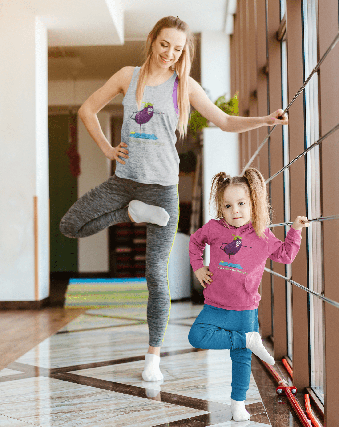 A toddler in a Rabbit Skins hoodie stands on one leg, smiling, with a purple eggplant design. Features jersey-lined hood, side pockets, and durable stitching for cozy wear.