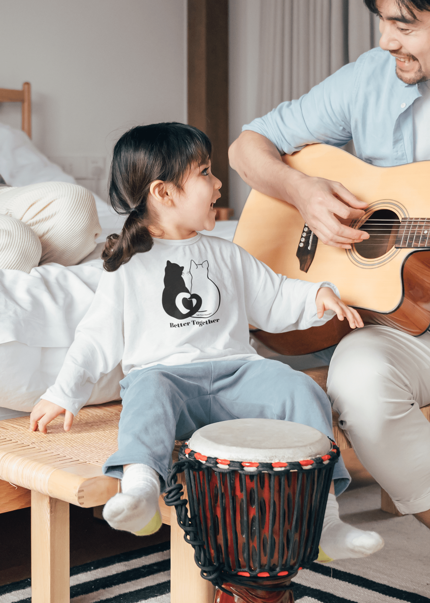 Toddler wearing Better Together Cat Love Tails Long Sleeve, sitting with a guitar-playing adult. Features durable, comfy cotton with EasyTear™ label for sensitive skin.