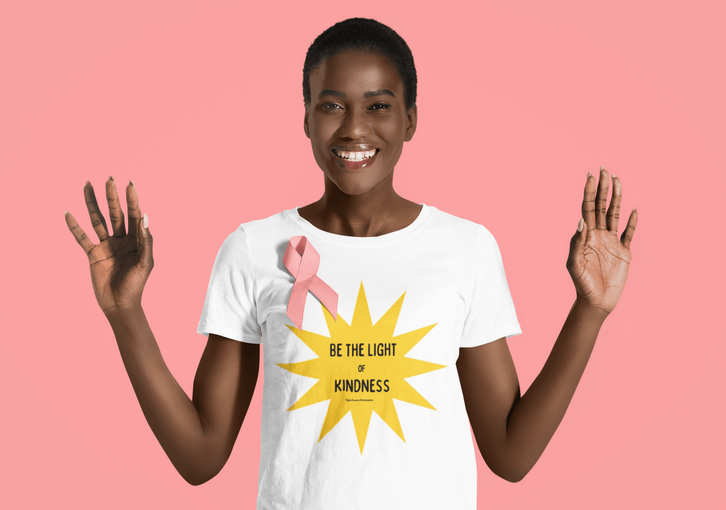 Woman wearing The Light Love and Peace Love Others Be the Light of Kindness T-shirt with a pink ribbon, smiling warmly.
