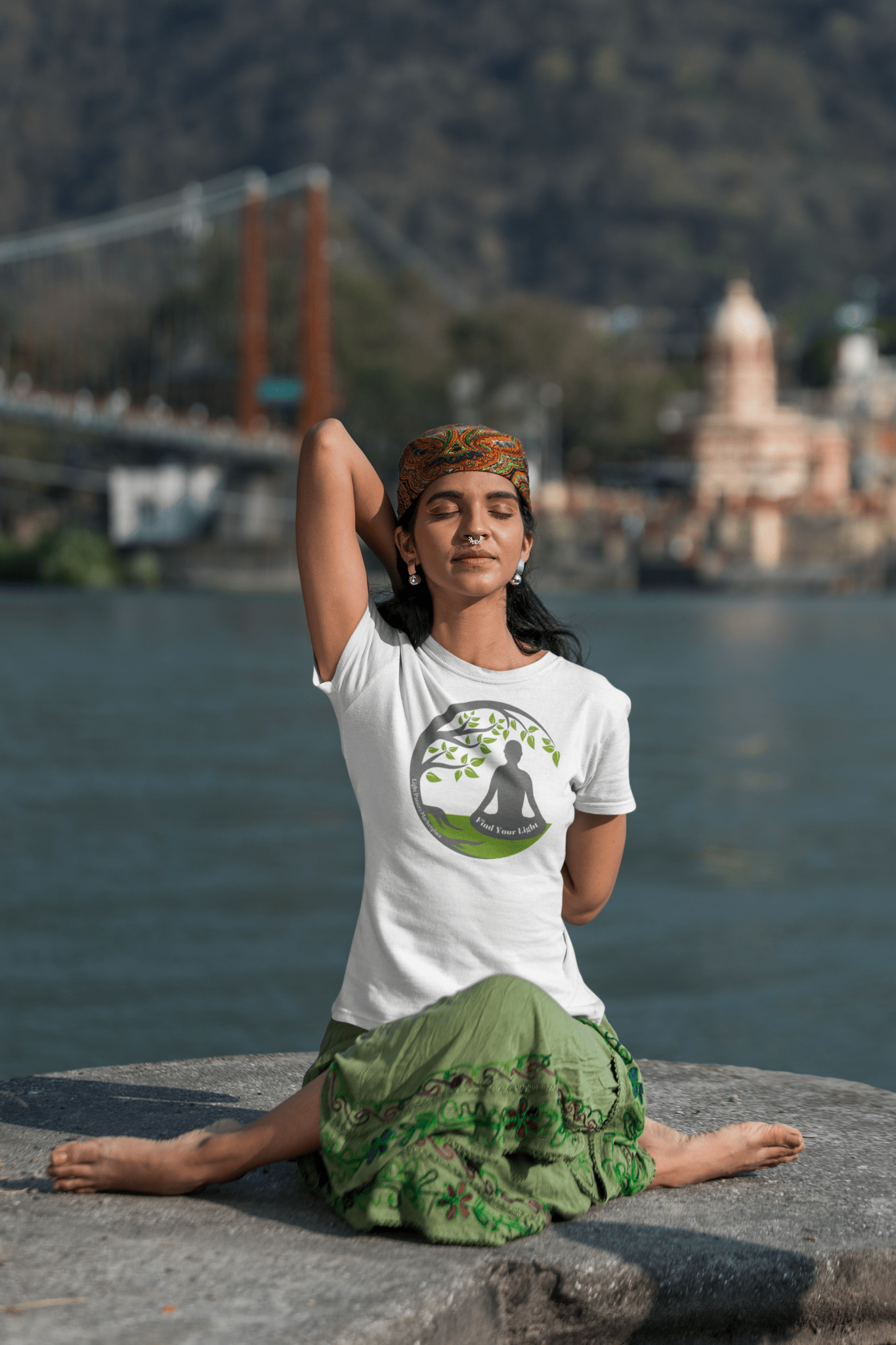 A woman sits on a rock by water, wearing a Meditation Unisex T-Shirt. Made of soft 100% cotton, featuring twill tape shoulders and ribbed collar. Ethically crafted with US cotton.