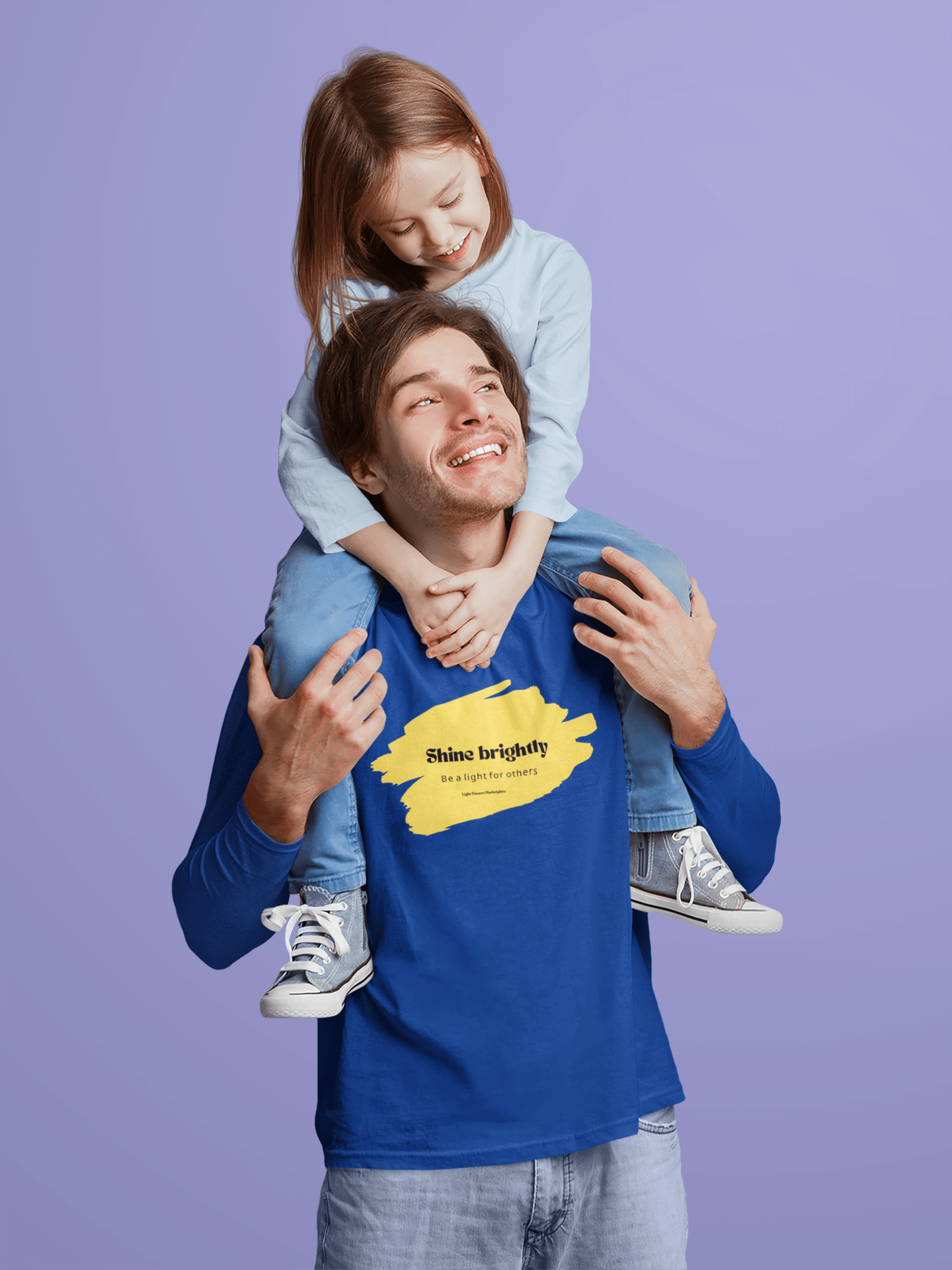 Man wearing The Light Adult Unisex Long Sleeve Tee, carrying a smiling girl on shoulders, showcasing the tee's uplifting message of spreading positivity.