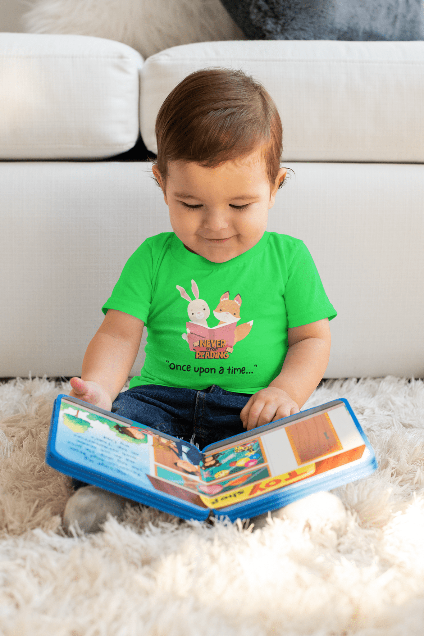 A toddler in a green shirt sits on the floor, engrossed in a book. This infant tee boasts durability and comfort with ribbed knitting and taped shoulders for a perfect fit.