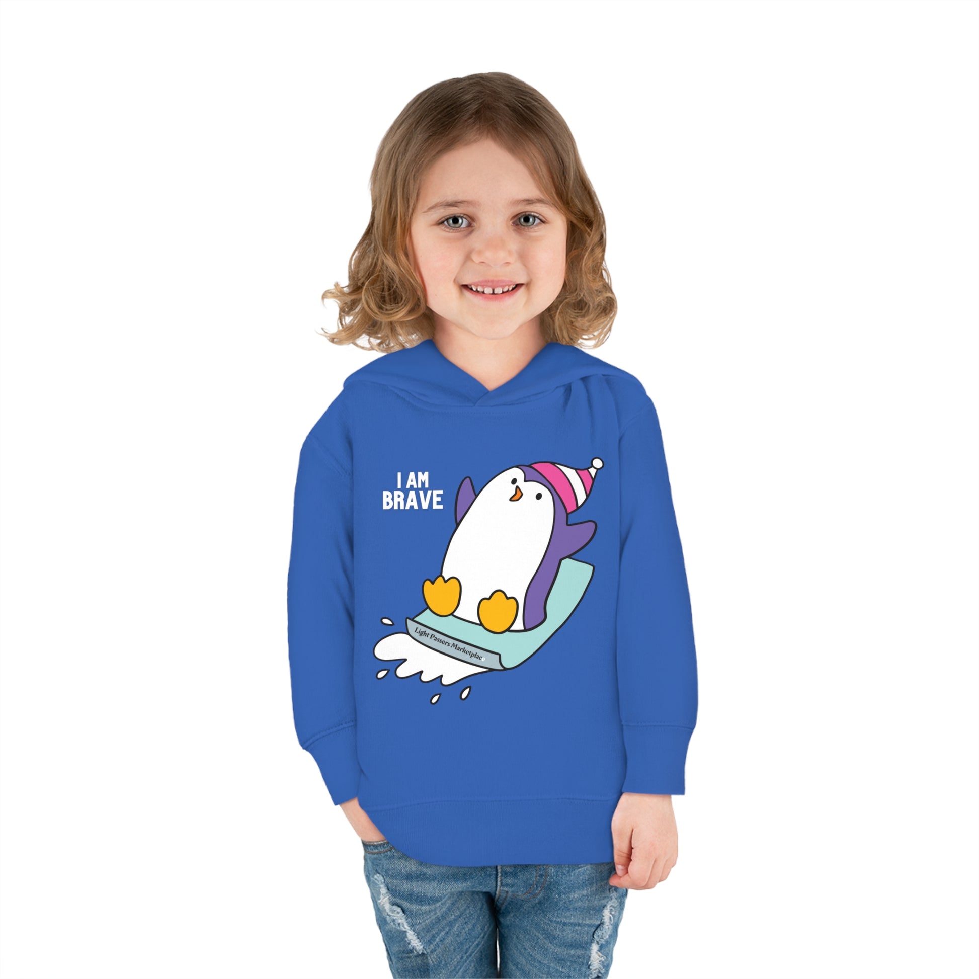 A child in a Rabbit Skins Brave Penguin Toddler Hooded Sweatshirt, smiling, with a penguin design, showcasing jersey-lined hood, cover-stitched details, and side seam pockets for cozy durability.