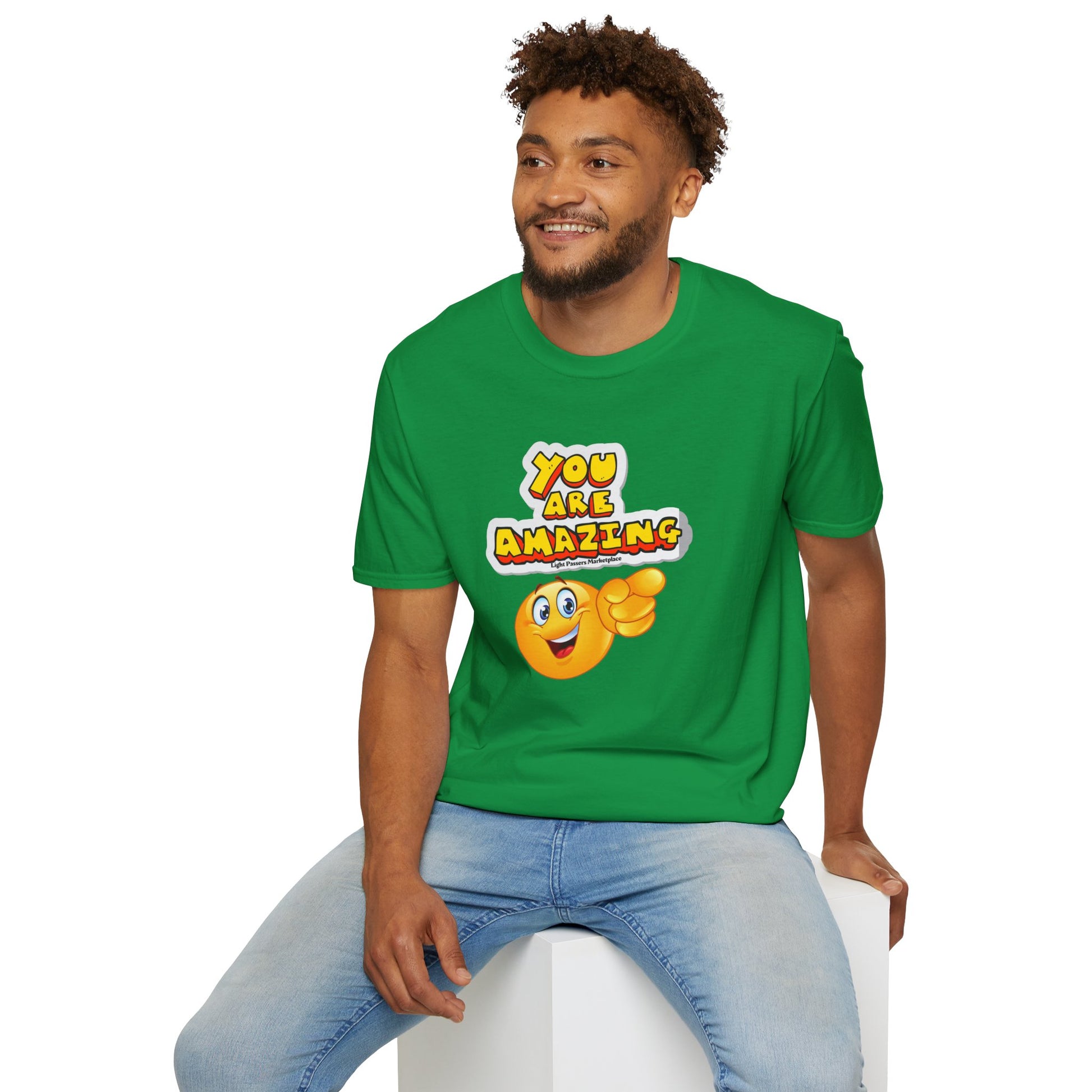 A man in a green shirt sits on a cube, smiling. Unisex soft-style t-shirt made of 100% cotton, featuring twill tape shoulders for durability and a clean crew neckline.