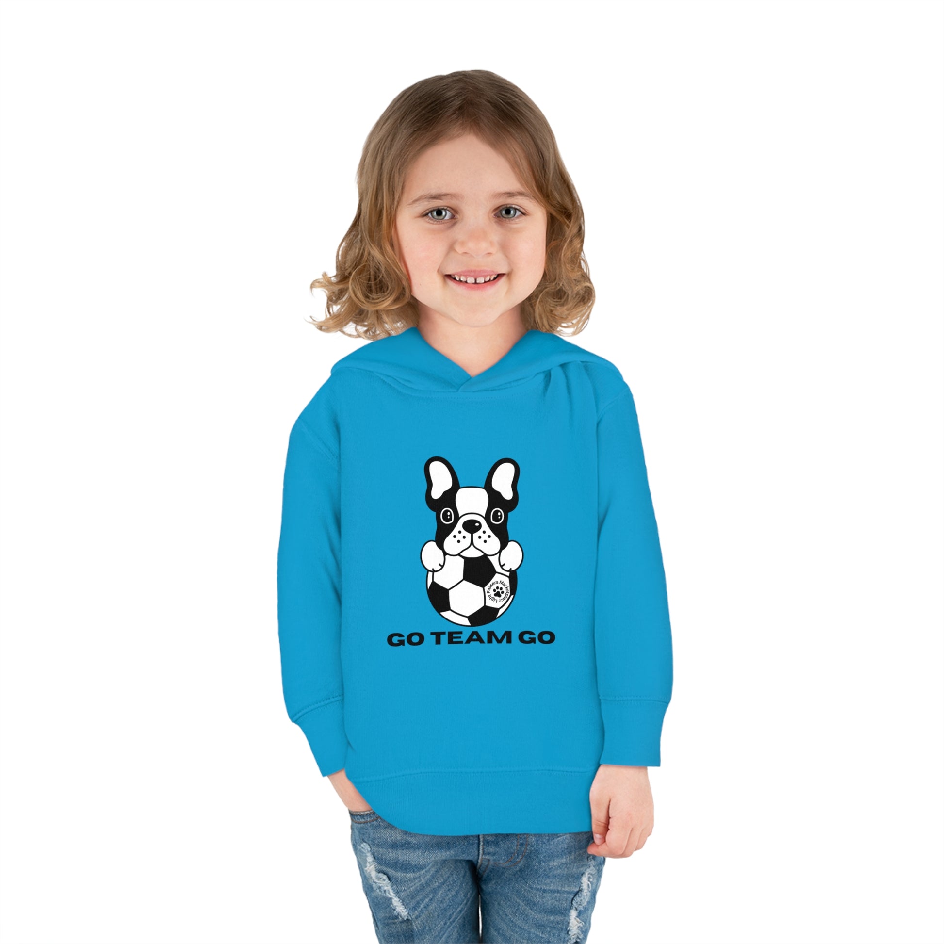 A child in a blue dog-themed toddler hoodie smiles, with a black and white dog holding a football in the background. Features jersey-lined hood, cover-stitched details, and side seam pockets for comfort and durability.