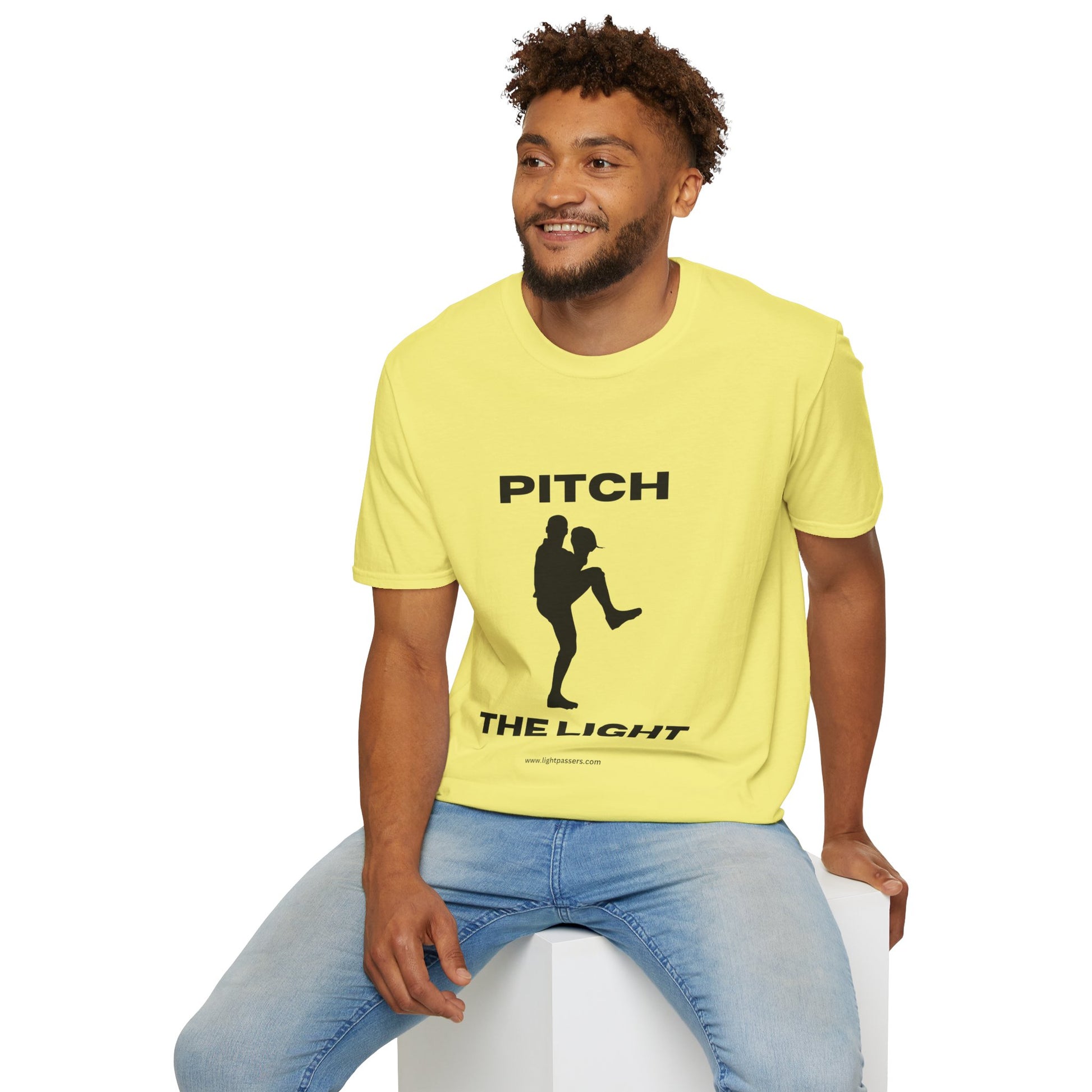 A man in a yellow shirt sits on a cube, showcasing the PITCH The LIGHT white lettering Unisex T-Shirt. Soft cotton, twill tape shoulders, tear-away label, Eurofit, no side seams.