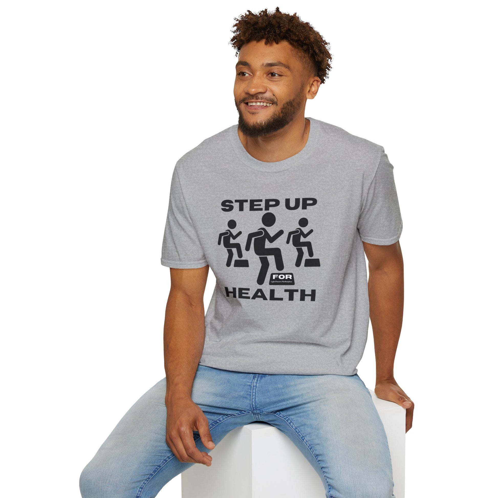 A man in a grey Step Up For Health unisex t-shirt sits on a cube. The tee, made of soft cotton, features twill tape shoulders and a ribbed collar. Ethically produced with ring-spun cotton.