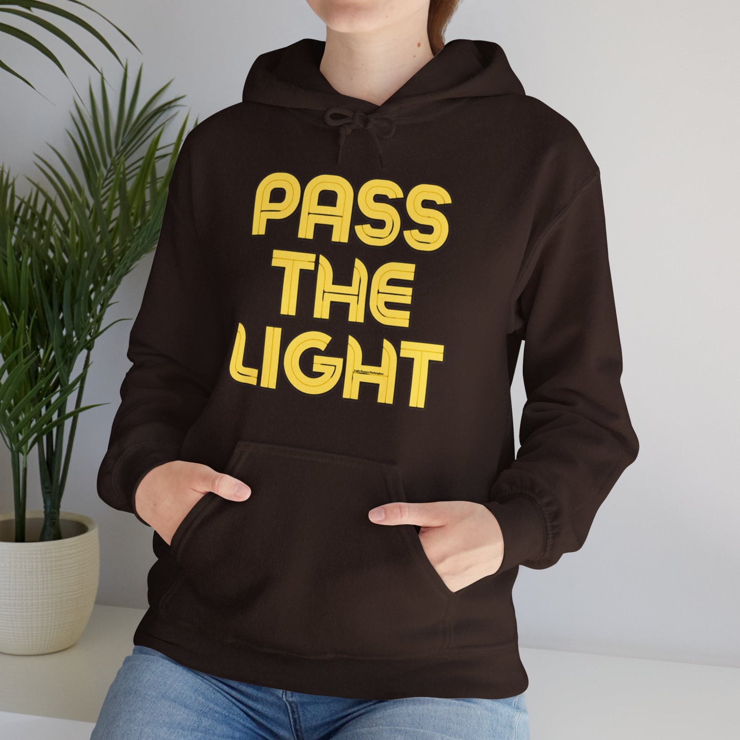 A person wearing a black hoodie with yellow text, featuring a kangaroo pocket and color-matched drawcord. Made of 50% cotton, 50% polyester blend for warmth and comfort.