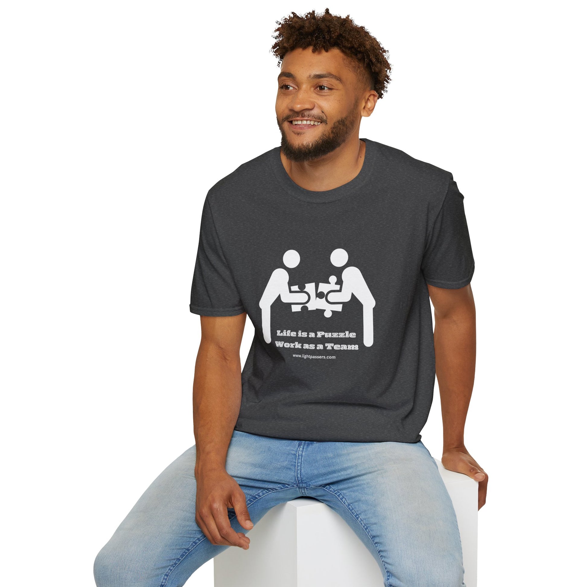 A man in a Life is a Puzzle Team Unisex T-shirt, sitting on a cube. Casual, heavy cotton tee with smooth surface for vivid printing. No side seams for comfort.