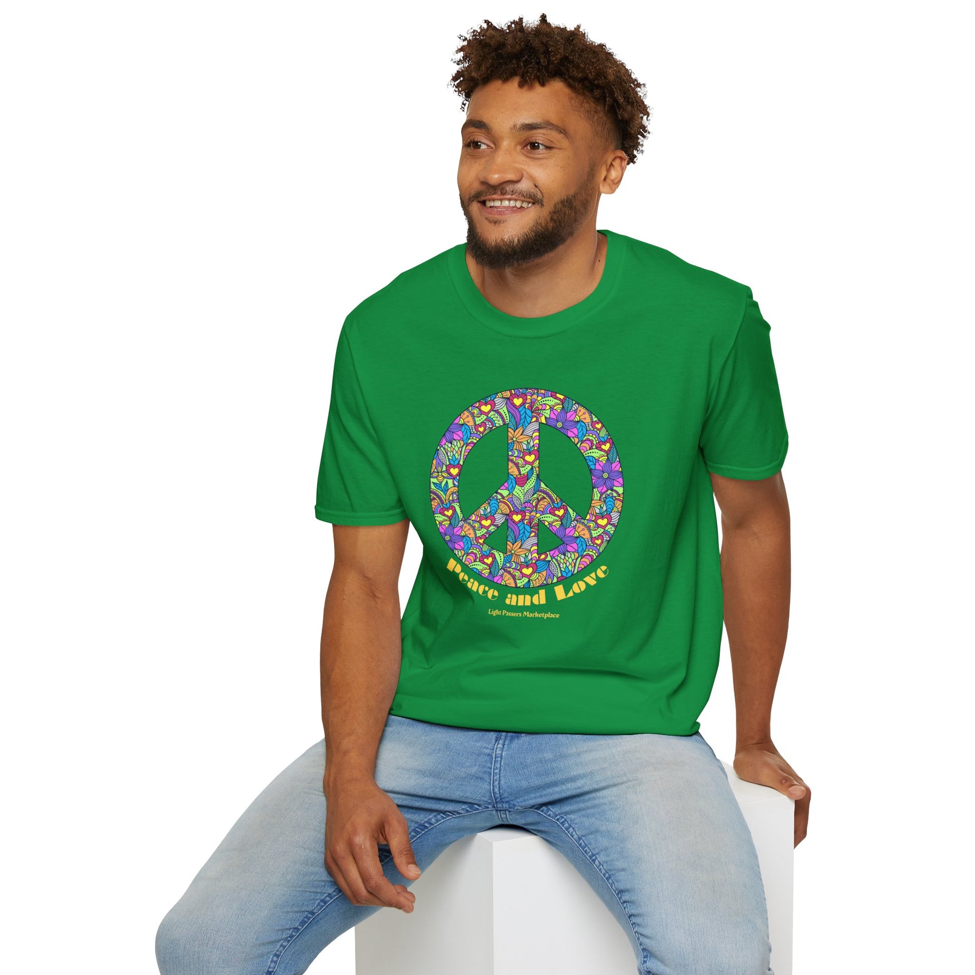 A man in a green Peace sign with flowers Unisex T-shirt, sitting on a cube. Made of soft 100% cotton, featuring twill tape shoulders for durability and a tear-away label for comfort.