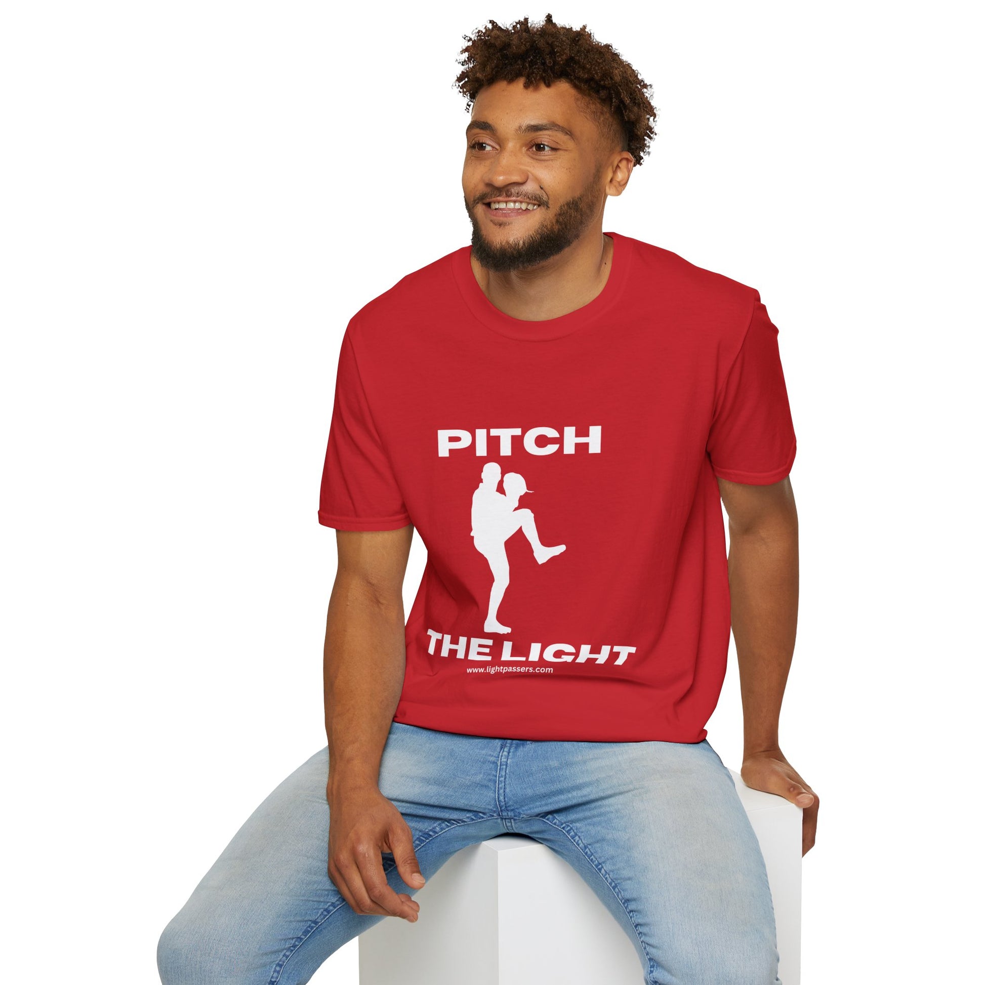 A man in a red shirt sits on a cube, showcasing the PITCH The LIGHT white lettering Unisex T-Shirt. Soft cotton, twill tape shoulders, no side seams, ribbed collar.