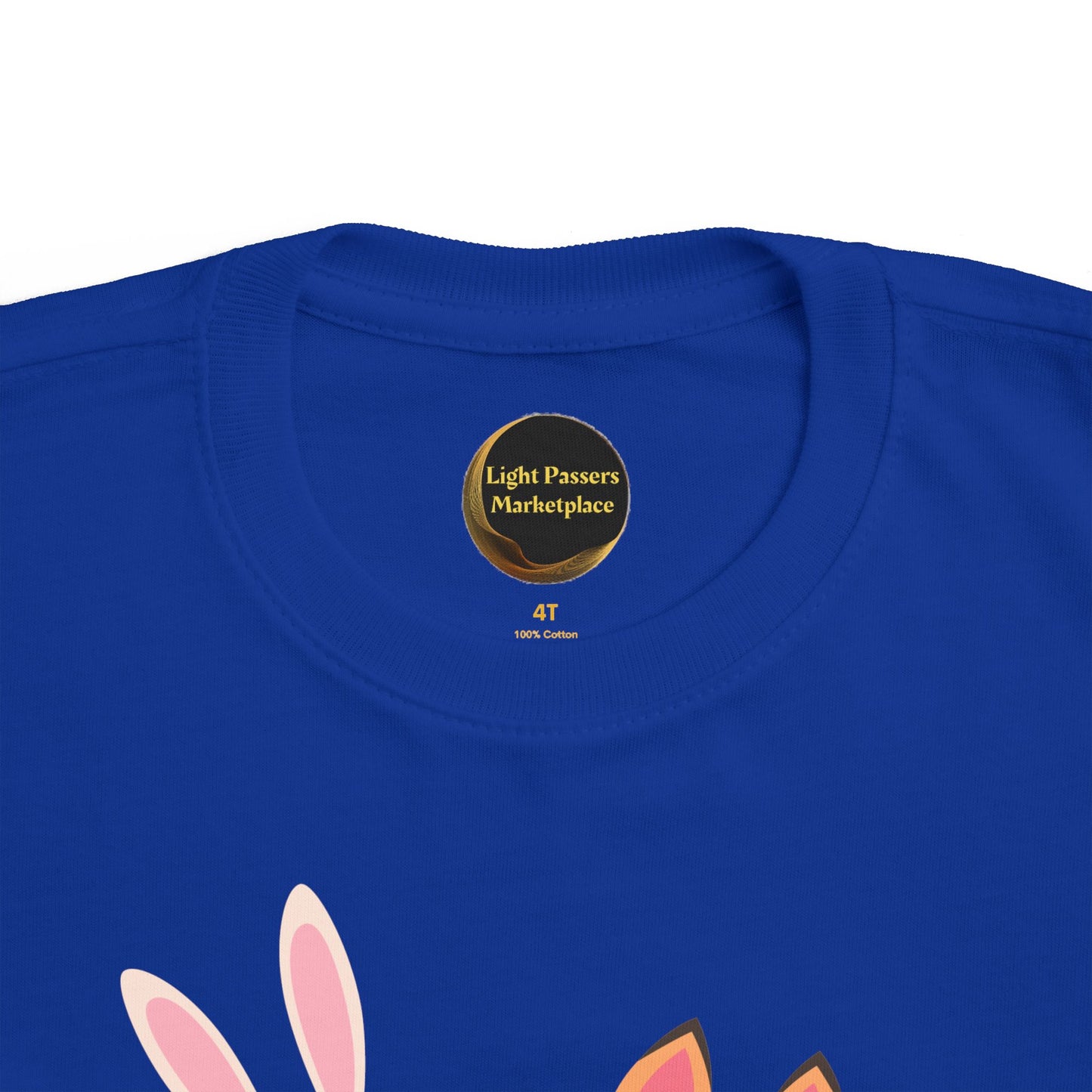 Close-up of a bright blue toddler tee neckline with Light Passers Marketplace label. Features bunny-ears design, representing The Light Never Stop Reading Toddler Tee — Two Bunnies Reading.