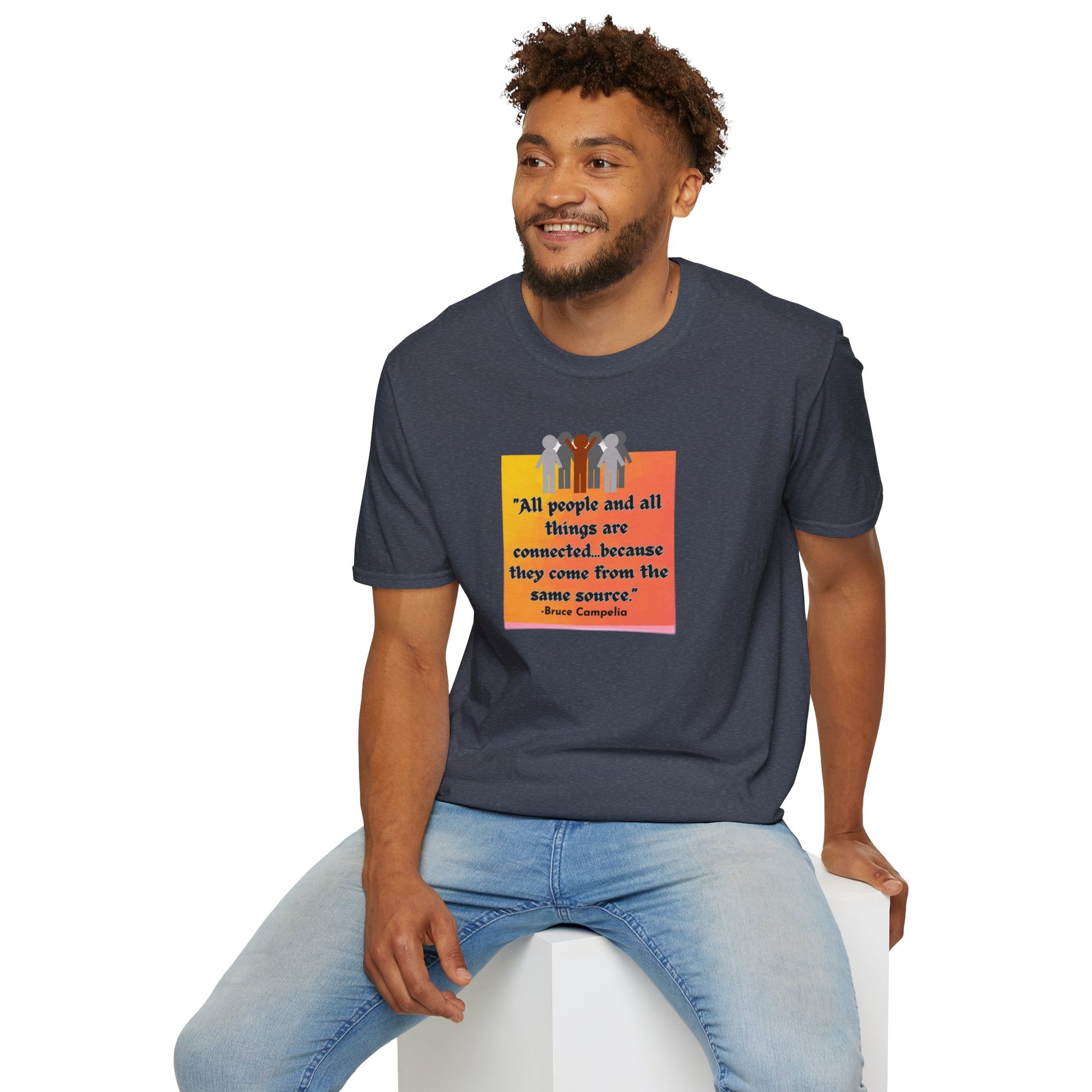 A man wearing a T-shirt, sitting on a white cube, surrounded by a group of people on a poster. Unisex heavy cotton tee with smooth surface for premium printing.