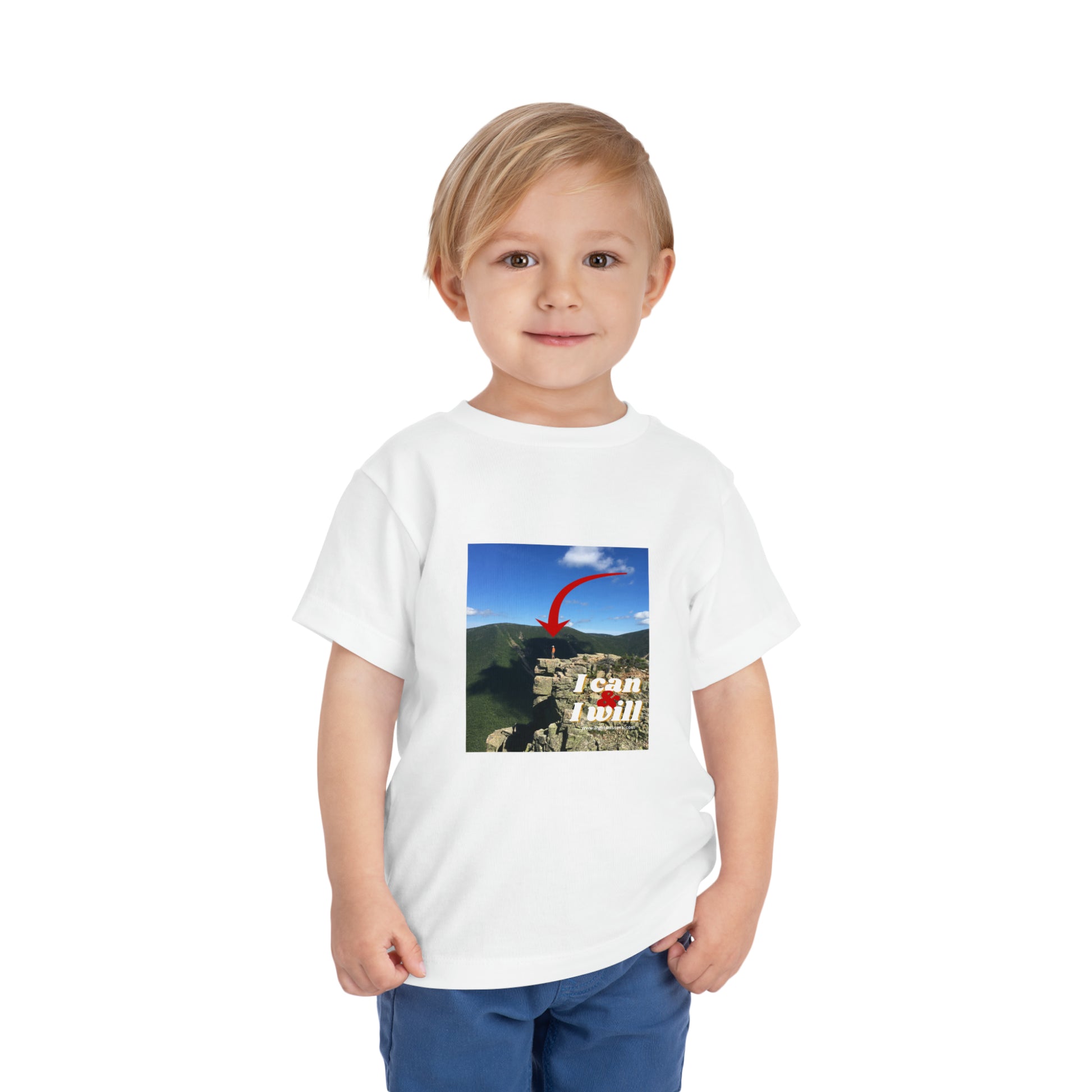 A determined toddler in a white I Can and I Will Hiking tee, standing confidently. Bella Canvas cotton shirt, tear-away label, 3.9 oz fabric.