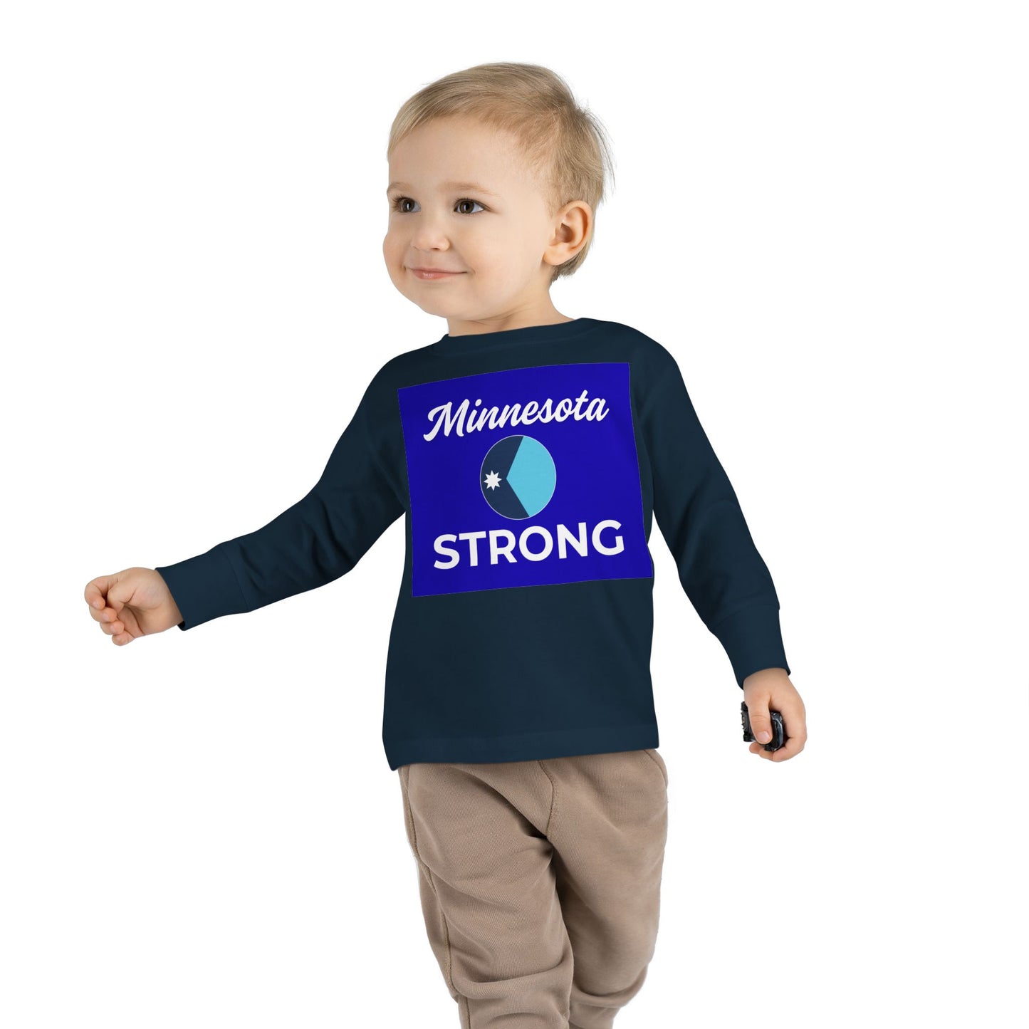 Toddler wearing Minnesota Strong navy long-sleeve tee and beige pants, holding a toy, embodying community pride and comfort from Light Passers Marketplace.