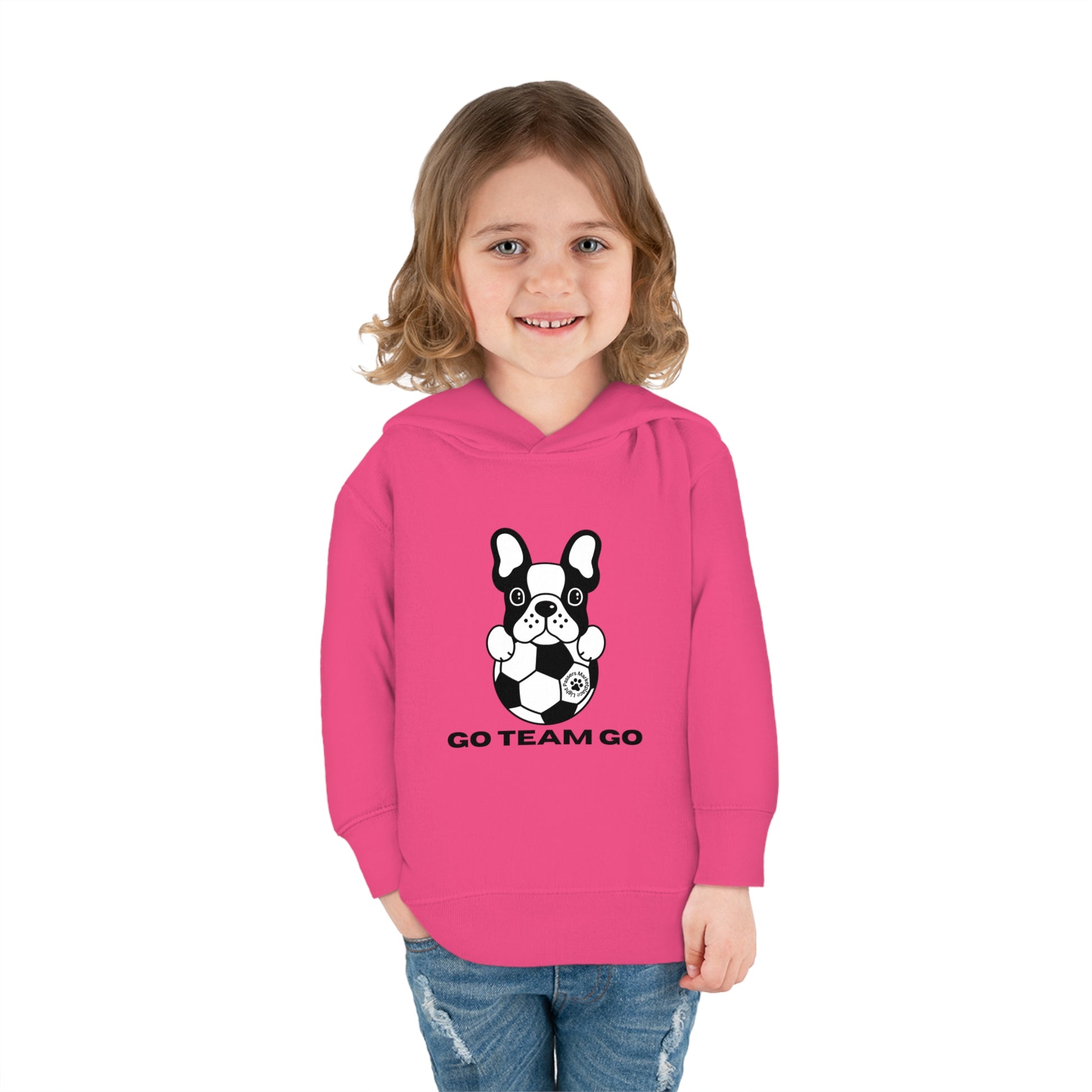 A toddler wearing a Soccer Dog Go Team Go hooded sweatshirt with a dog and football design. Features jersey-lined hood, side seam pockets, and durable stitching for lasting coziness.