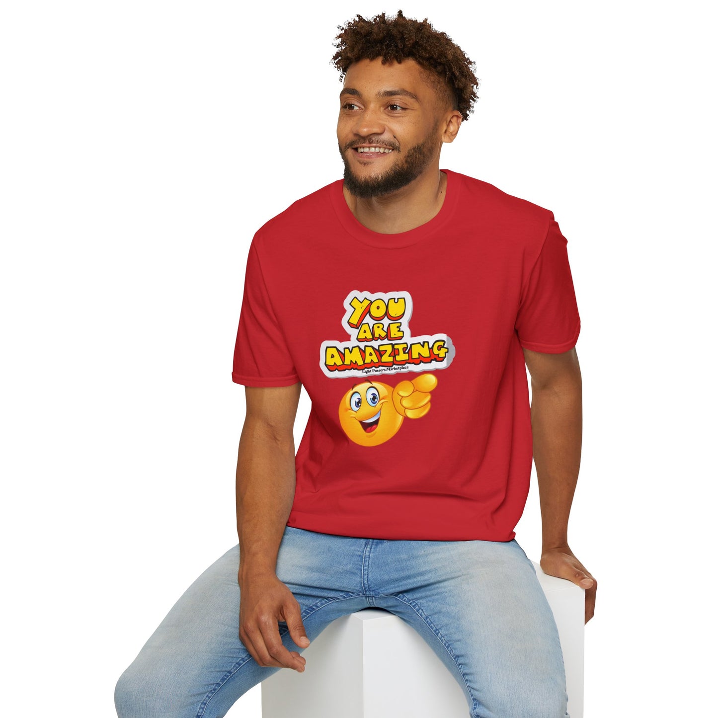 A man in a red shirt sits on a cube, smiling. Unisex soft-style tee made of 100% cotton, with twill tape shoulders for durability. Comfortable, versatile, and ethically produced.