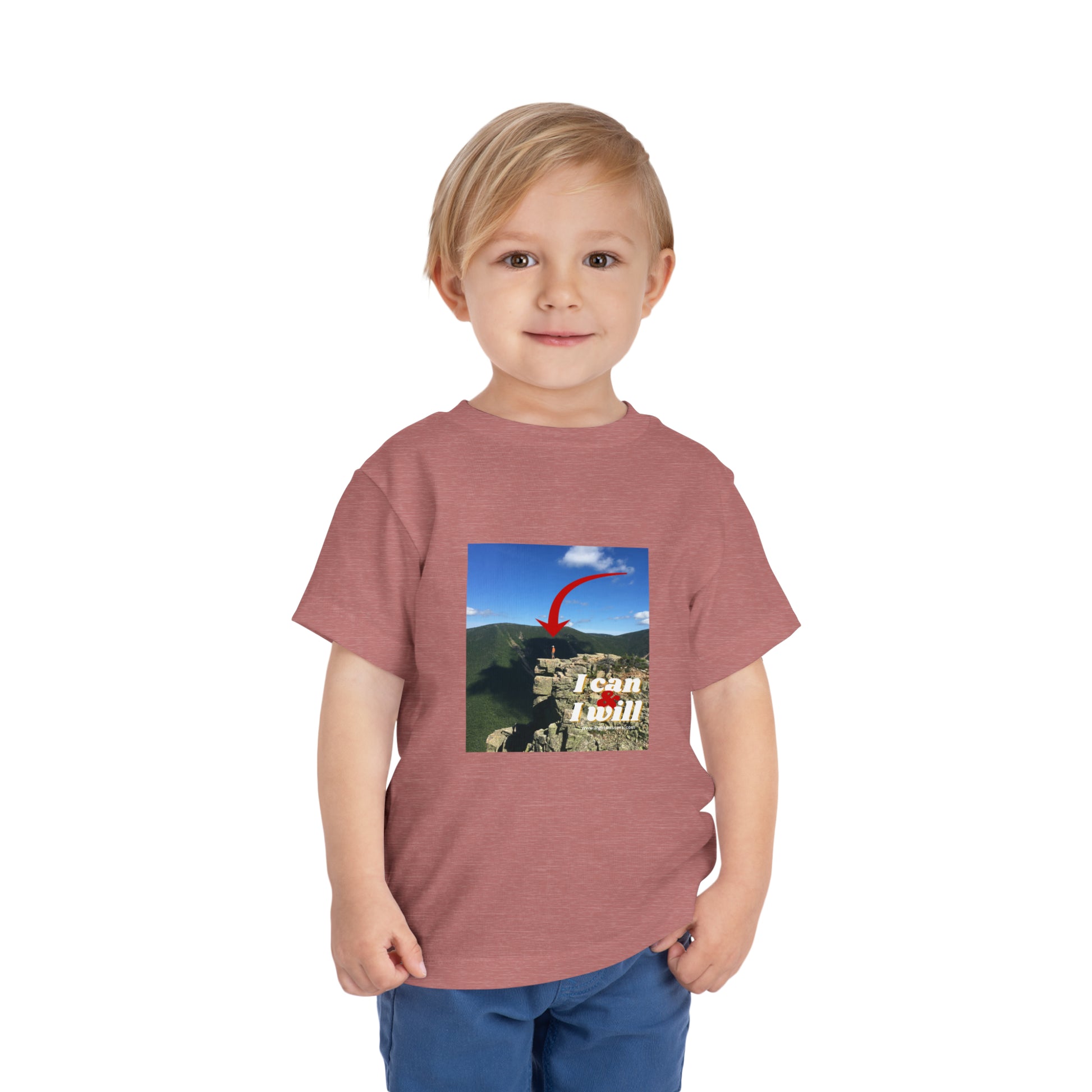 A toddler in a red shirt stands confidently on a cliff, embodying the spirit of the I Can and I Will Hiking Toddler T-shirt. Made of 100% Airlume cotton for comfort and style.