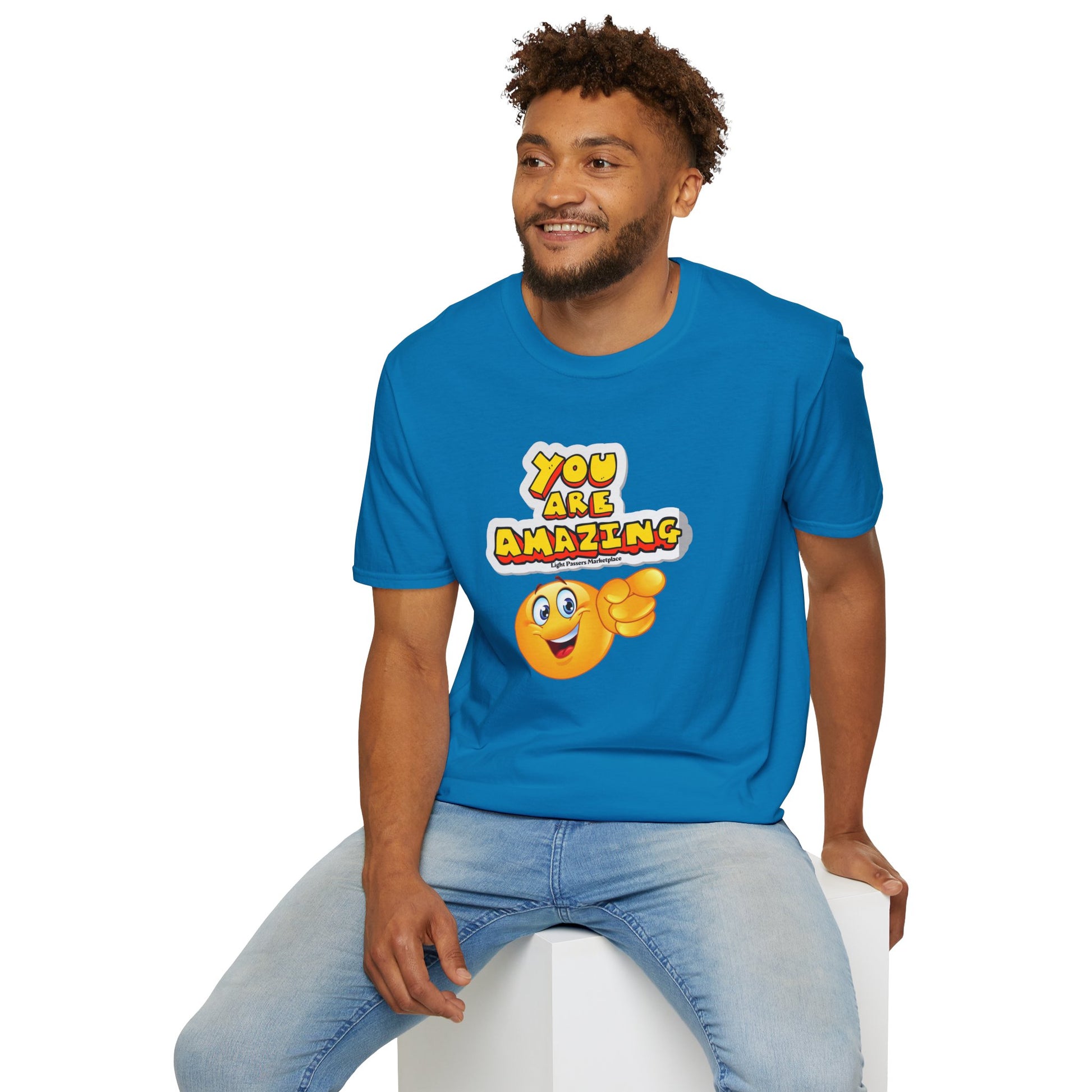 A man in a blue shirt sits on a cube, a yellow cartoon character points. Unisex soft-style tee, 100% cotton, twill tape shoulders, no side seams, ribbed collar.