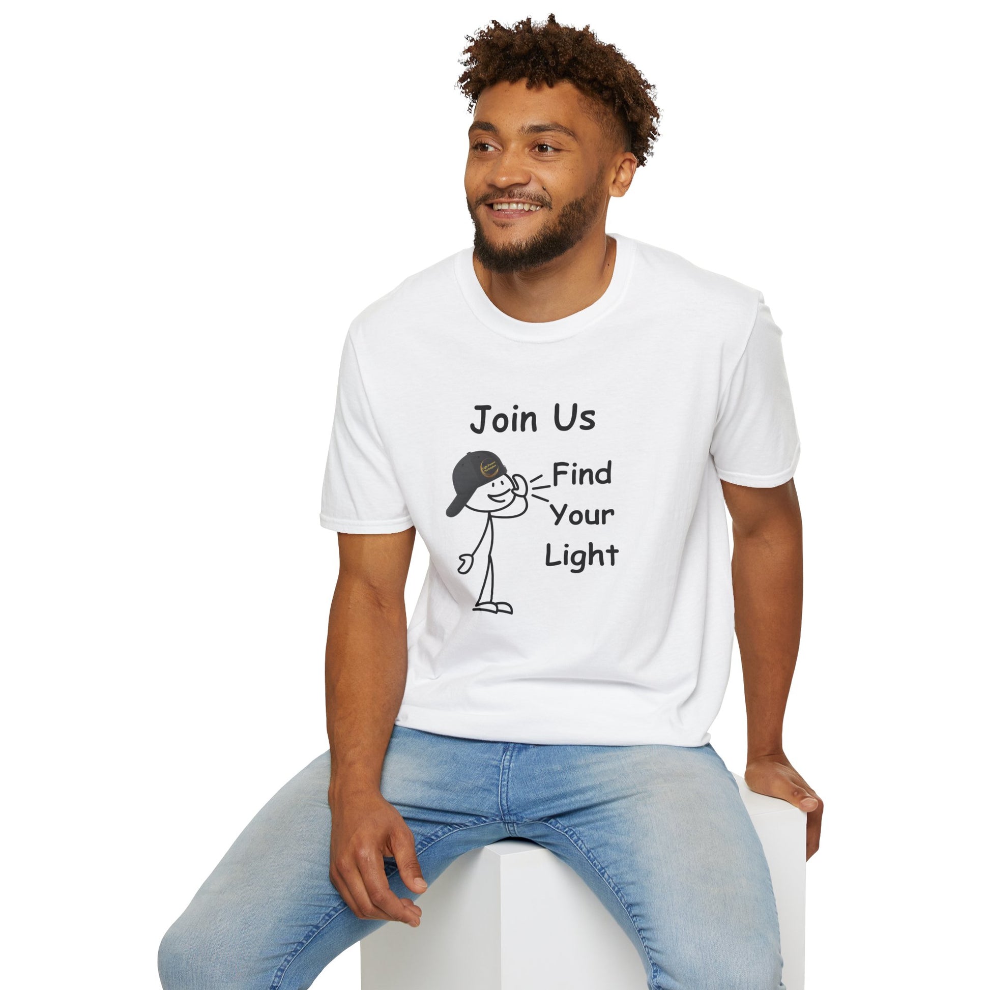 A man in a white shirt sits on a cube, showcasing the Join Us Find Your Light Unisex T-Shirt. Made of soft 100% cotton, featuring twill tape shoulders and a ribbed collar for durability and comfort.