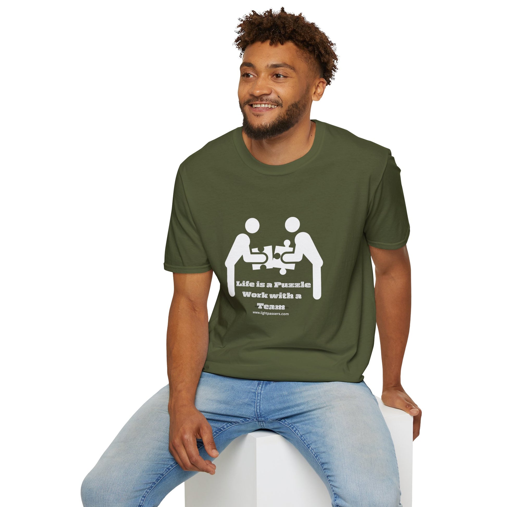 A man in a green shirt sits on a cube, smiling with a beard. Unisex heavy cotton tee with puzzle piece design. 100% cotton, no side seams, tear-away label.