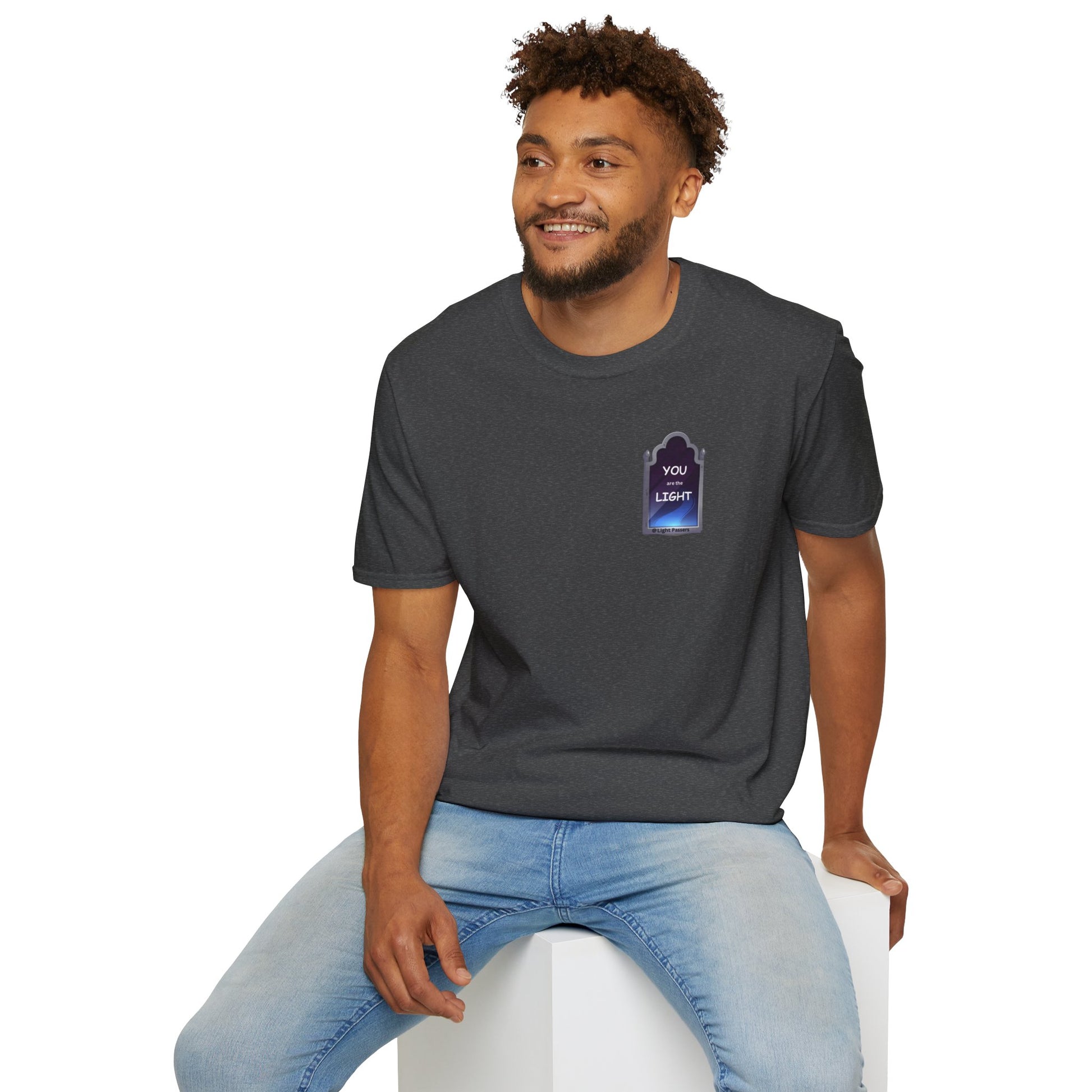 A man in a grey shirt sits on a cube, showcasing the YOU ARE THE LIGHT small Mirror Unisex T-shirt. The tee offers a classic fit, 100% cotton fabric, and tear-away label for comfort.