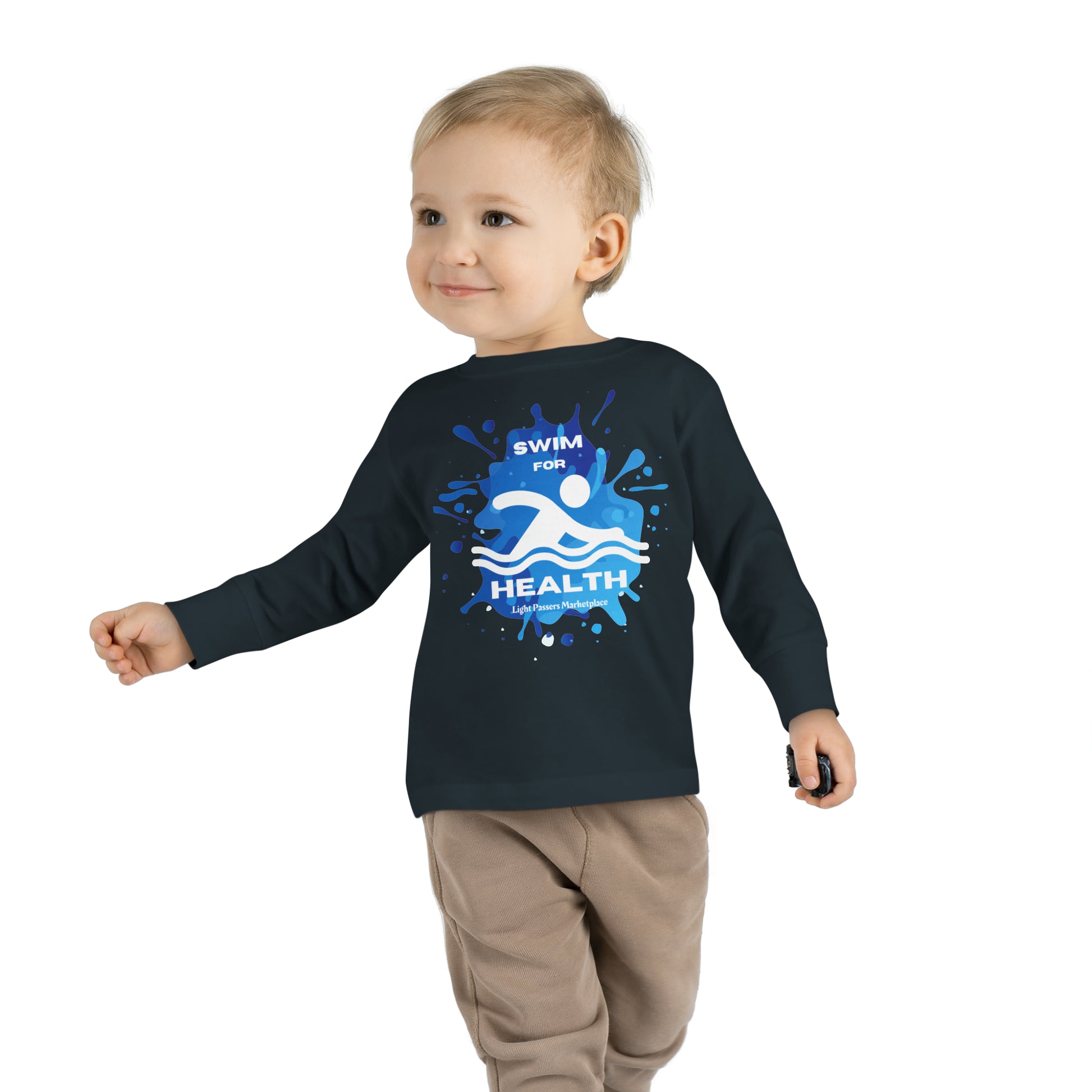 A child in a Swim for Health Toddler Long Sleeve T-shirt, featuring a logo and paint splashes, walking towards the camera. Made from 100% combed ringspun cotton, with ribbed collar and tear-away label for comfort and durability.