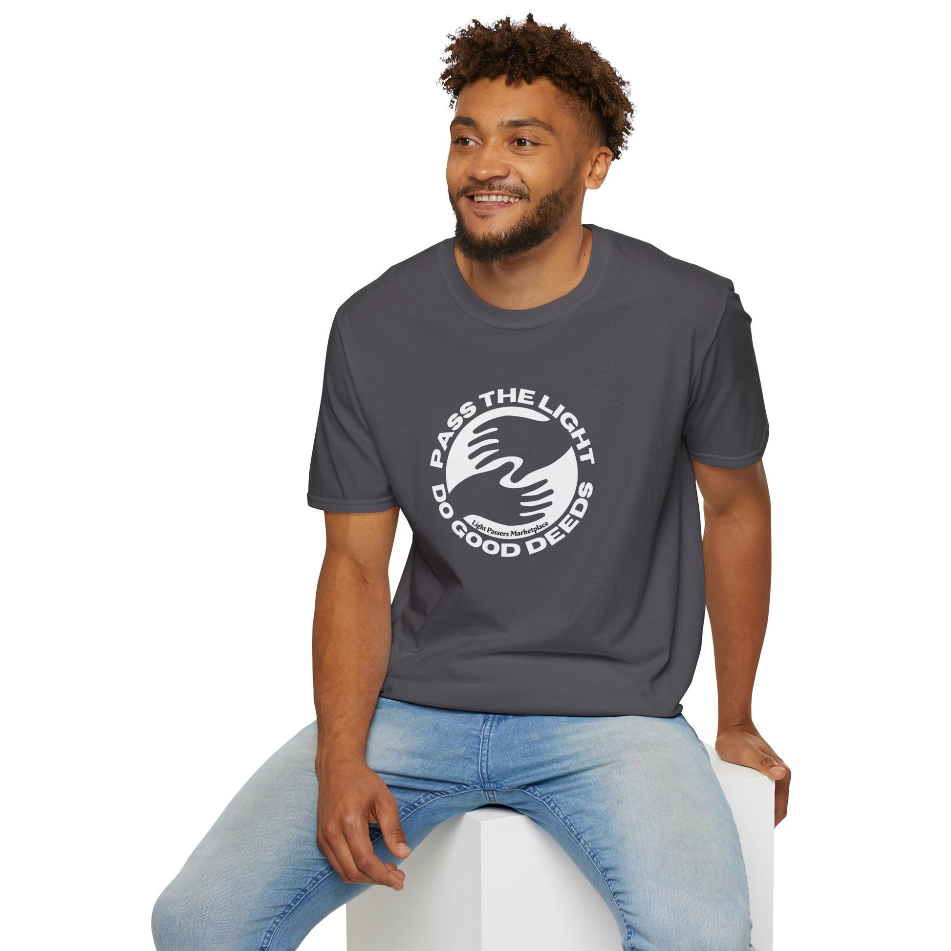 A man in a grey shirt sits on a cube, showcasing the Pass the Light Do Good Deeds Unisex T-shirt. The image emphasizes the casual, versatile nature of the tee, ideal for everyday wear.