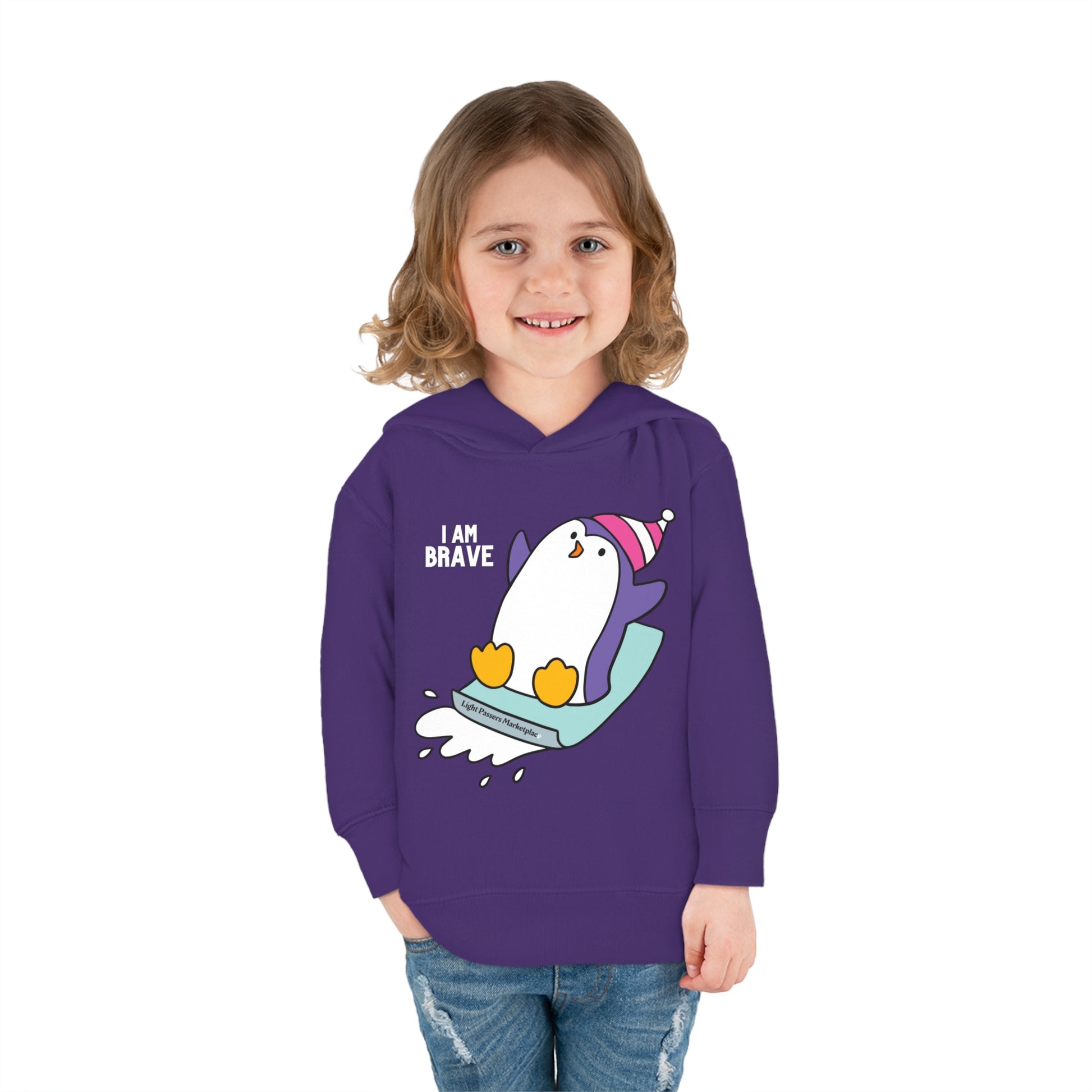 Toddler hoodie with a girl smiling, featuring a cartoon penguin design. Jersey-lined hood, cover-stitched details, side seam pockets for comfort and durability. Made of 60% cotton, 40% polyester.