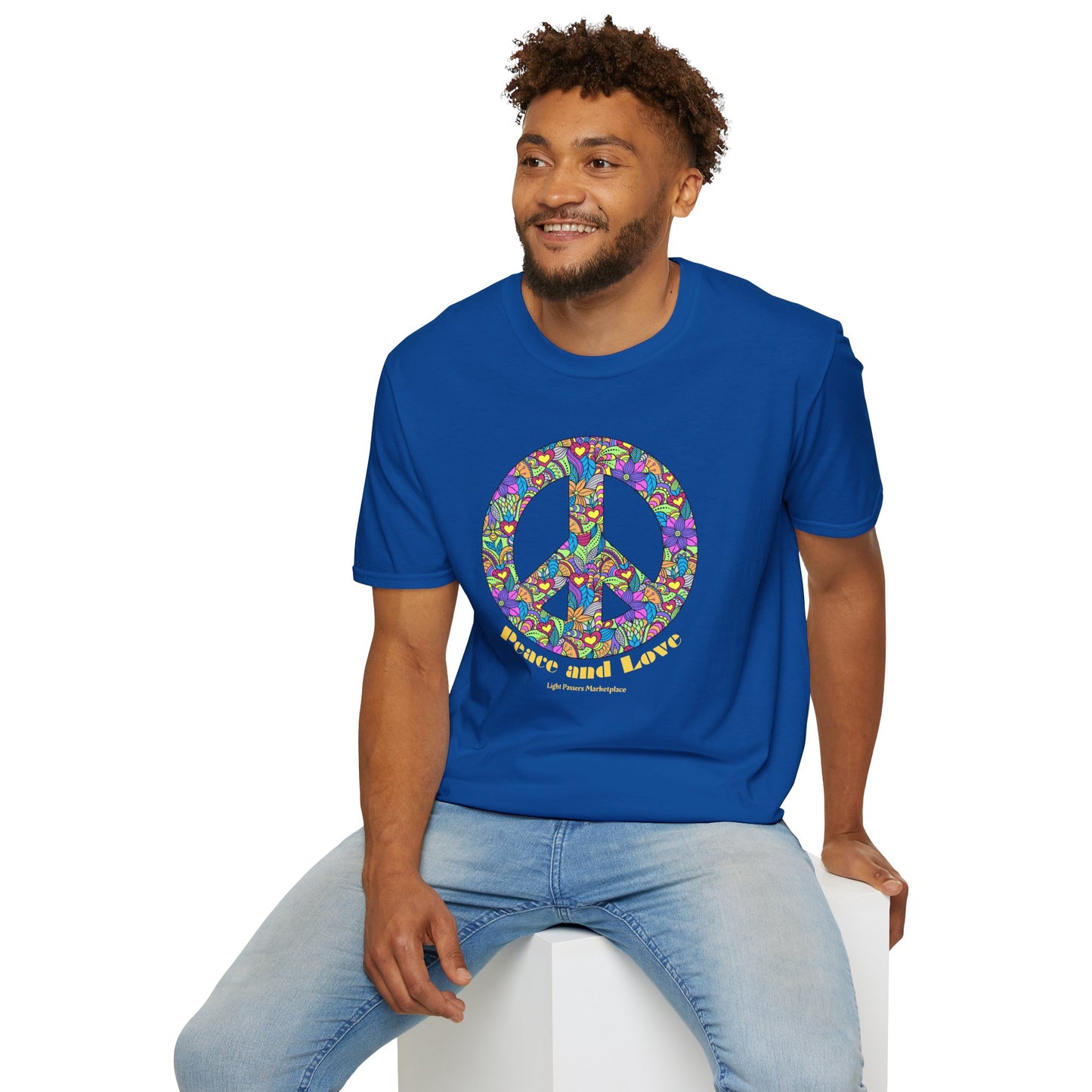 A man in a blue shirt with a peace sign sits on a cube, showcasing the Peace Sign with Flowers Unisex T-shirt. Made of soft 100% cotton, featuring twill tape shoulders for durability and a clean crew neckline.