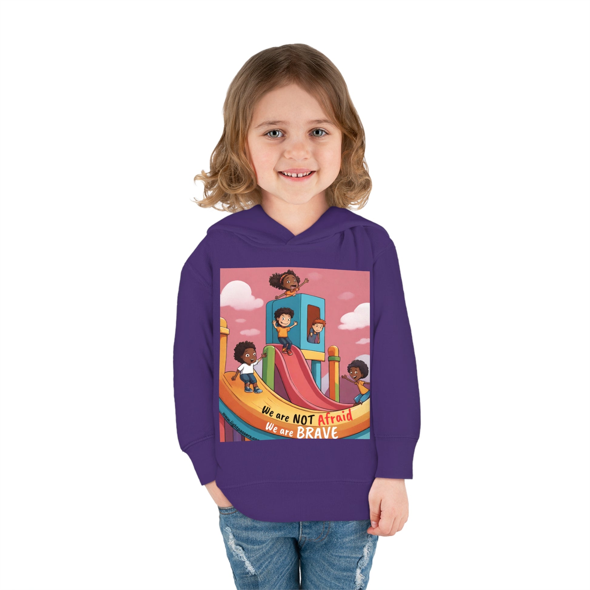 Toddler in Rabbit Skins hoodie with cartoon design, smiling. Features jersey-lined hood, cover-stitched details, side-seam pockets for cozy wear. We are Brave Toddler Hooded Sweatshirt for durable comfort.