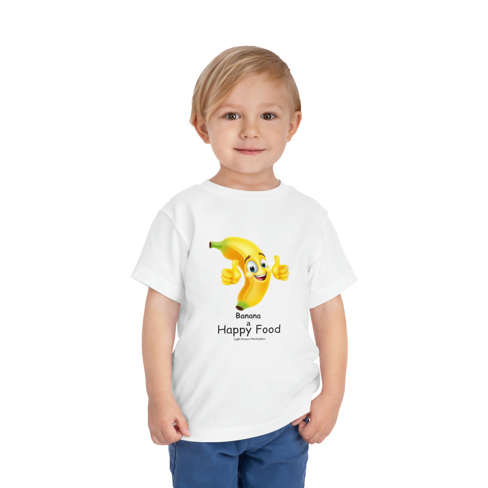 A toddler wearing a white Banana Happy Food t-shirt, featuring a cartoon banana giving a thumbs up. Made of 100% Airlume combed cotton for comfort.