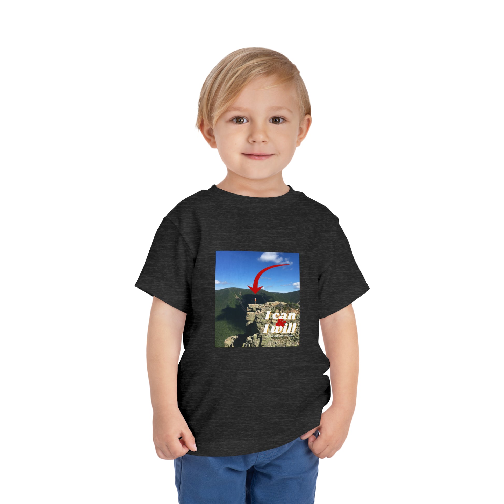 A determined boy in a black I Can and I Will Hiking toddler t-shirt, standing confidently. Made of 100% Airlume cotton, light fabric, tear-away label for comfort.