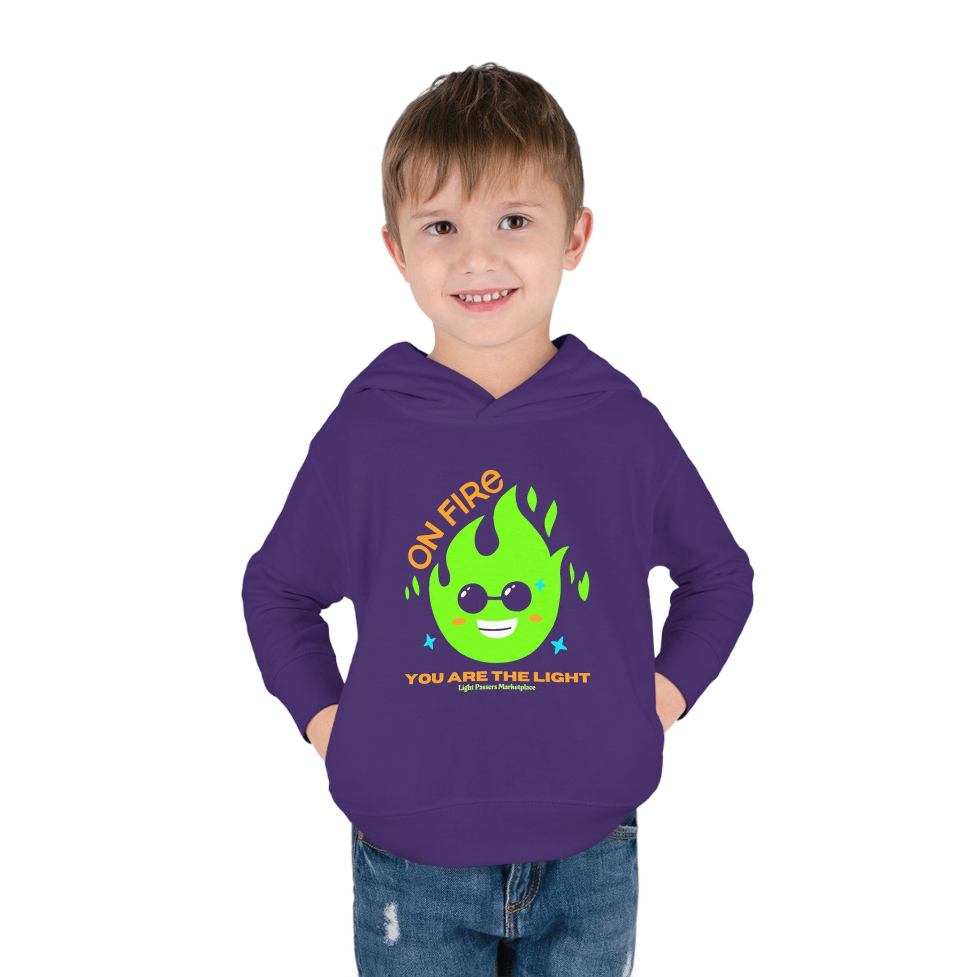 A toddler in a purple hoodie with a cartoon fire logo, green flame graphic, and yellow text. Features jersey-lined hood, side seam pockets, and durable stitching. Made of 60% cotton, 40% polyester blend.