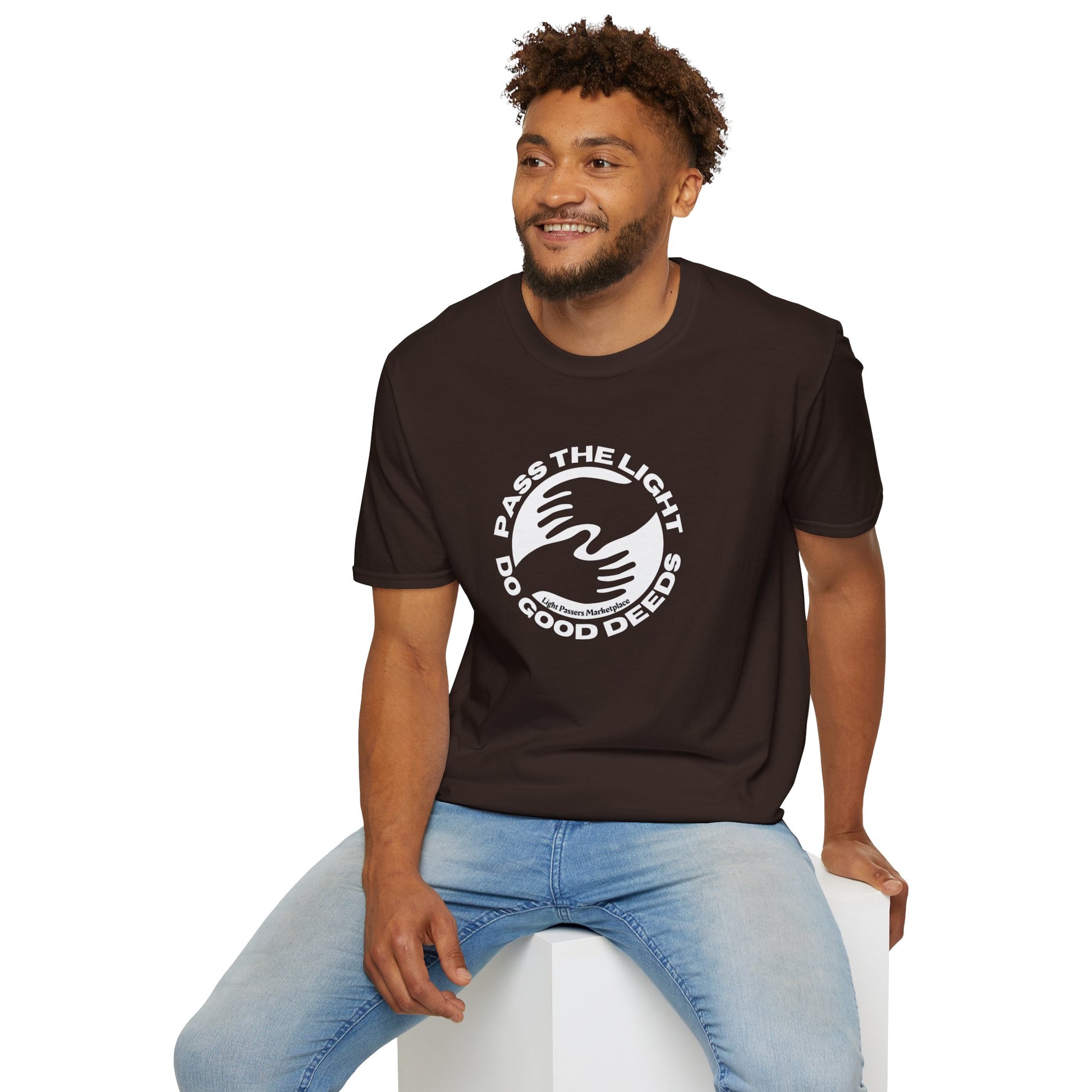 A man in Pass the Light Do Good Deeds Unisex T-shirt sits on a cube. Brown shirt, curly hair, smiling. No side seams for comfort. 100% cotton, tear-away label. Classic fit.