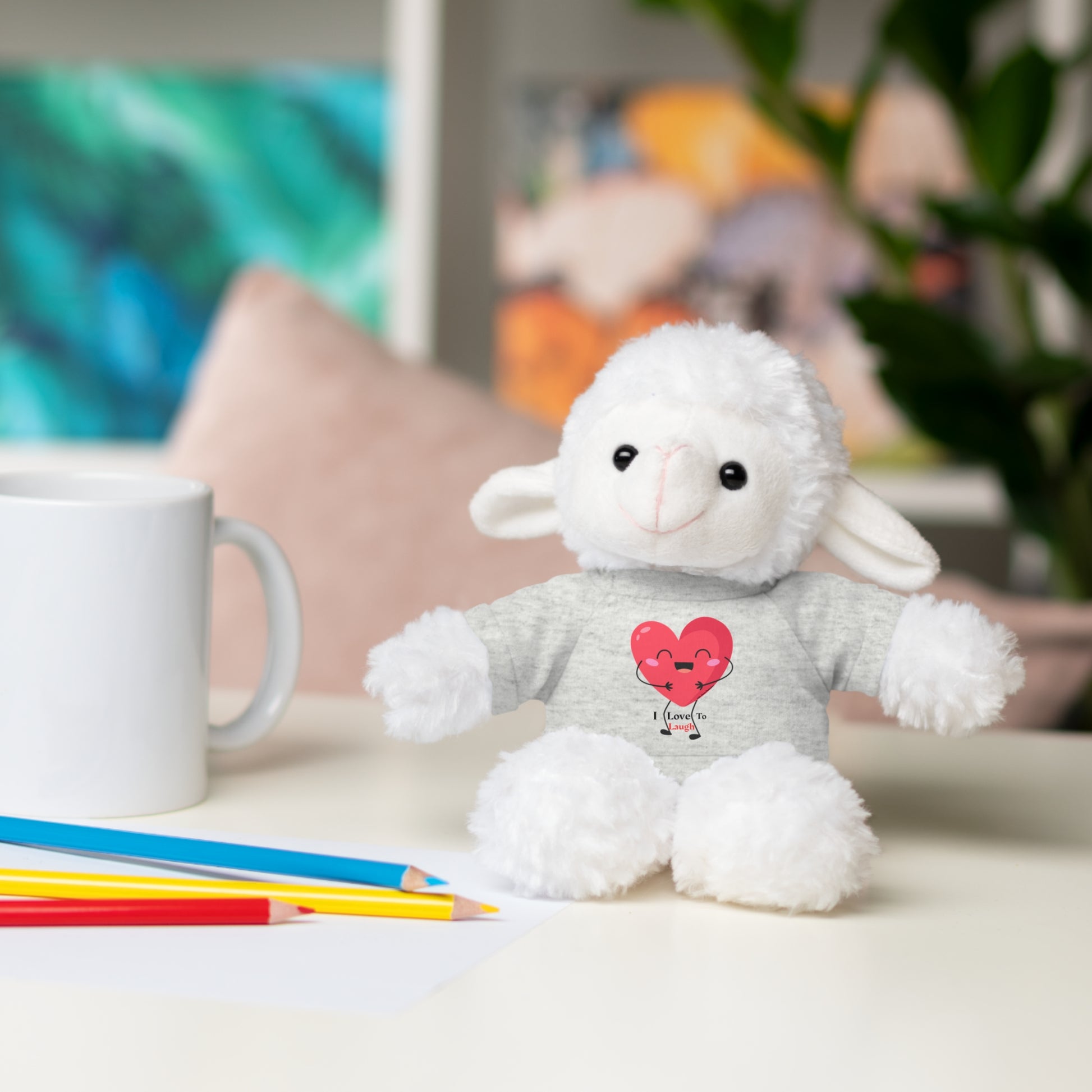 Stuffed animal with a removable I Love to Laugh heart shirt, sitting beside a mug on a table, from the Cool Stuff Stuffies collection.