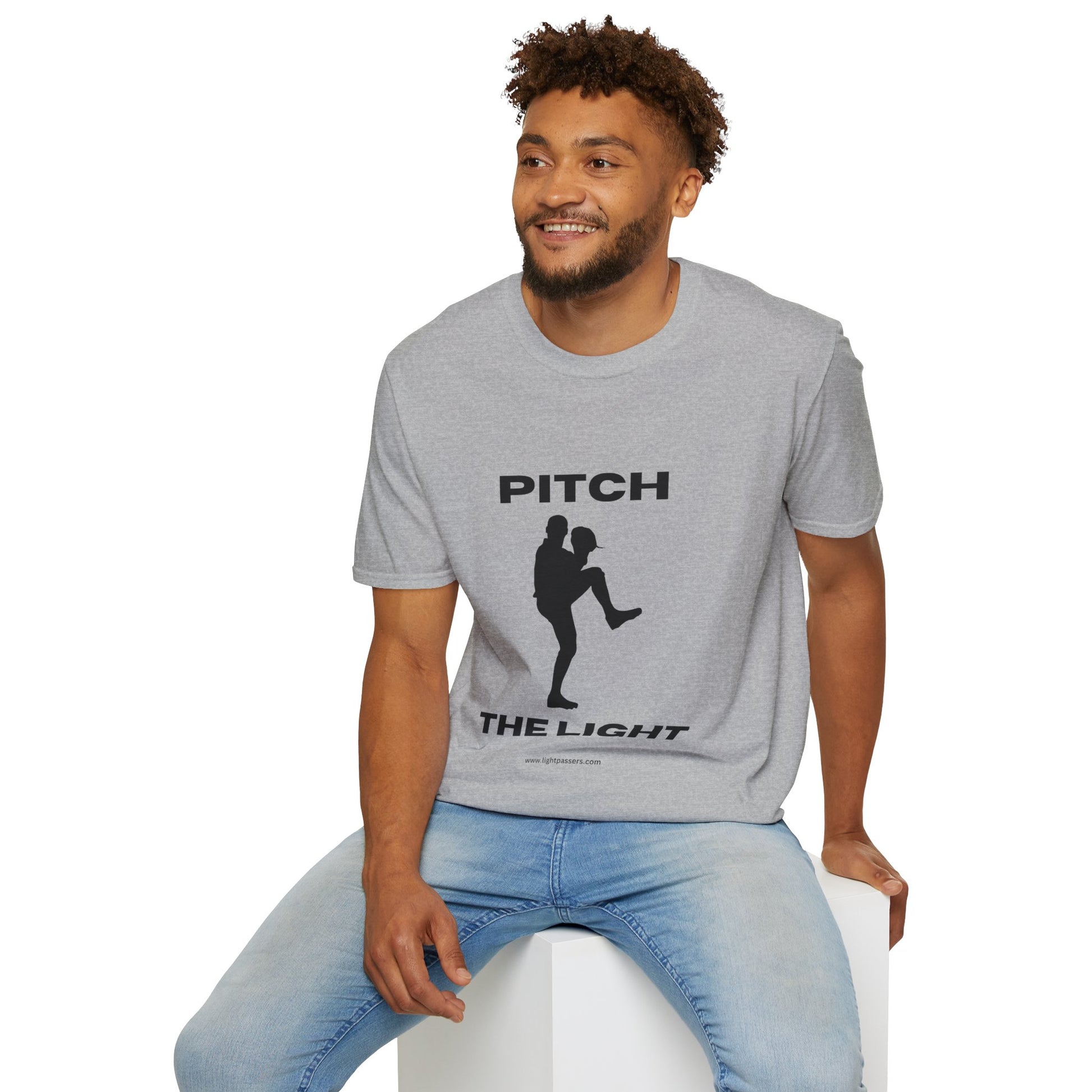 A man in a grey shirt sits on a cube, showcasing the PITCH The LIGHT white lettering Unisex T-Shirt. Soft 100% cotton, twill tape shoulders, no side seams, ribbed collar.