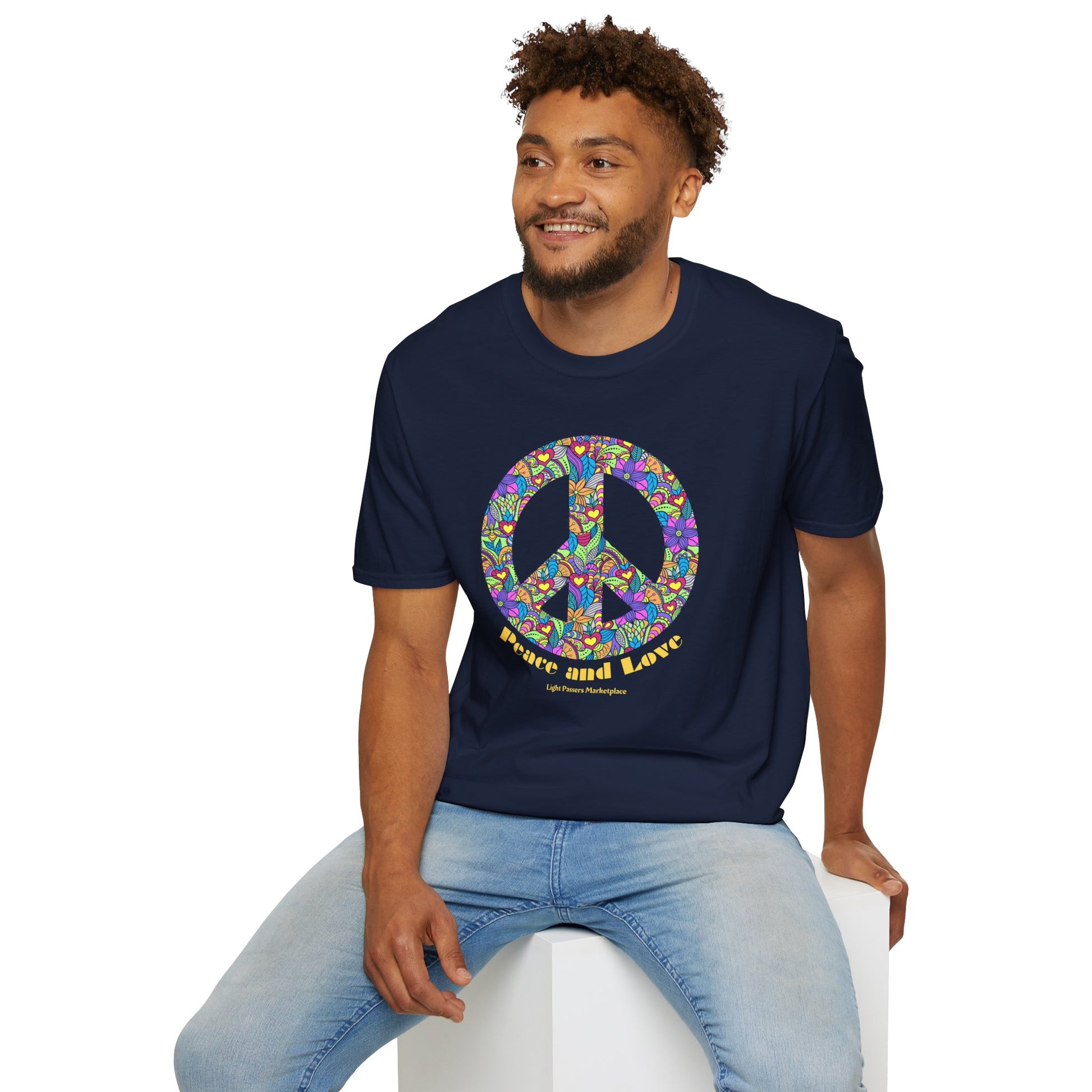 A man wearing a blue shirt with a peace sign sits on a cube, showcasing the Peace sign with flowers Unisex T-shirt. Made of soft 100% cotton, featuring twill tape shoulders for durability and a ribbed collar.