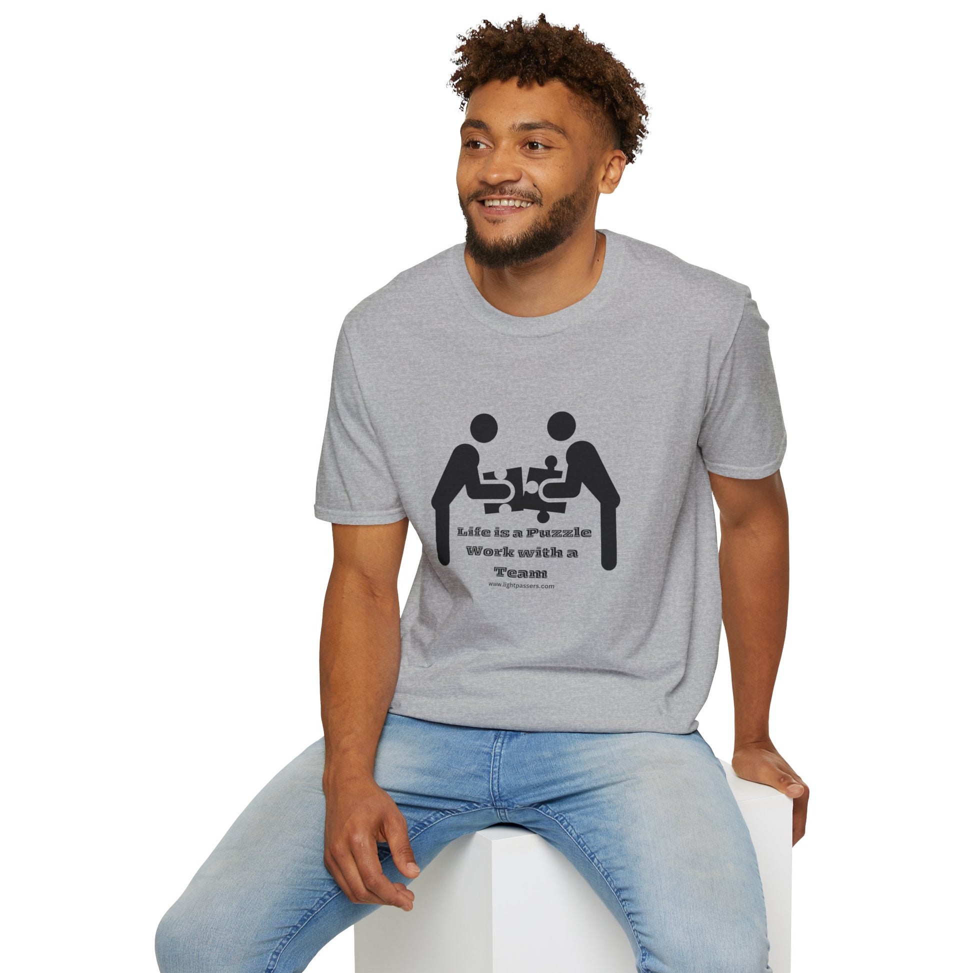 A man in a Life is a Puzzle Team Unisex T-shirt, sitting on a cube. Casual wear with smooth cotton fabric, no side seams, and durable shoulders. Classic fit for versatile style.