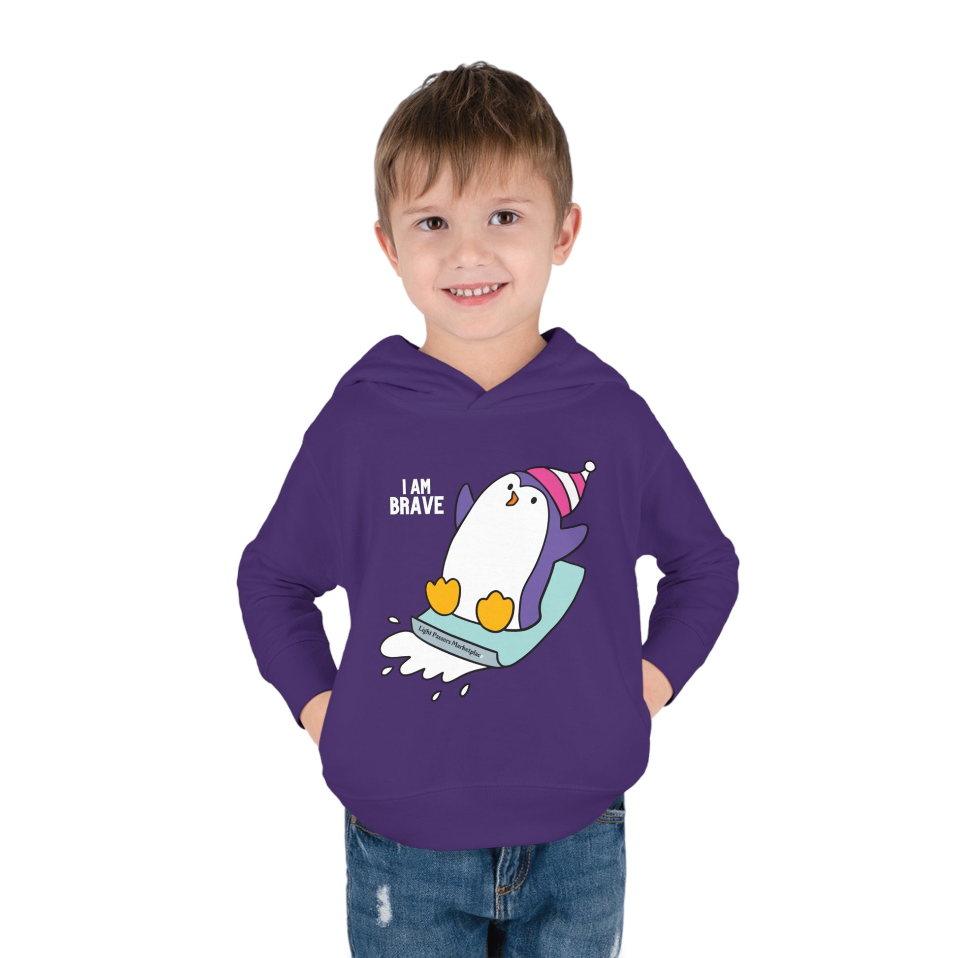 A toddler in a Rabbit Skins hoodie with a Brave Penguin design, featuring a jersey-lined hood, cover-stitched details, and side seam pockets for cozy wear.