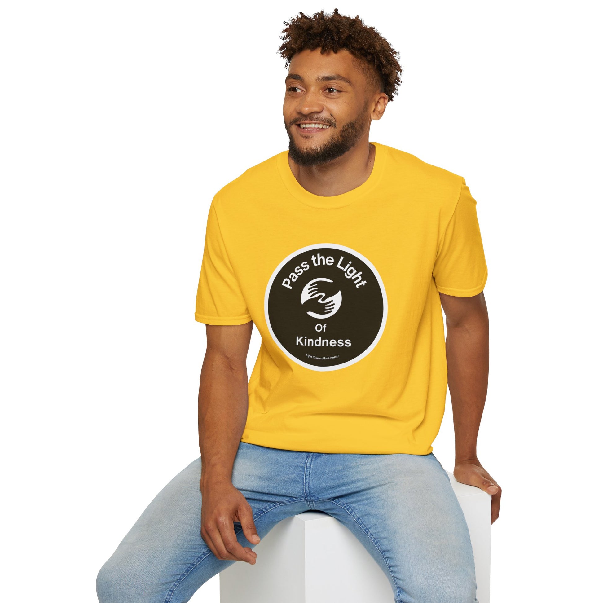 A man in a yellow shirt sits on a cube, showcasing the Pass the Light of Kindness 2 hands Unisex T-shirt. The heavy cotton tee offers a smooth surface for vibrant prints, with no side seams for comfort.