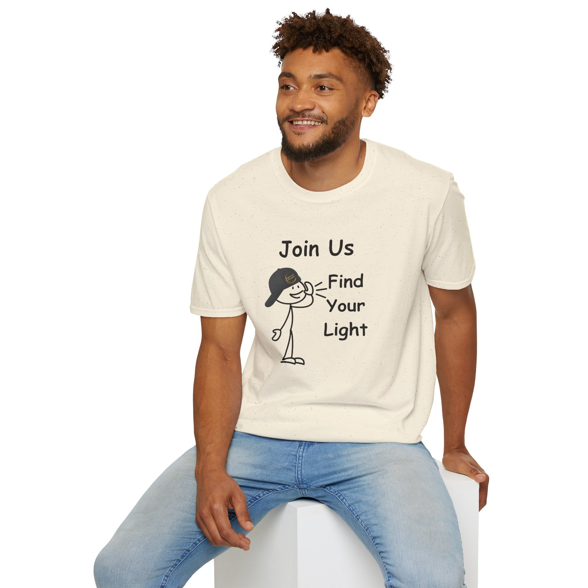 A man sits comfortably on a cube, wearing a white shirt. This Join Us Find Your Light Unisex T-Shirt offers casual comfort with 100% ring-spun cotton, twill tape shoulders, and no side seams.