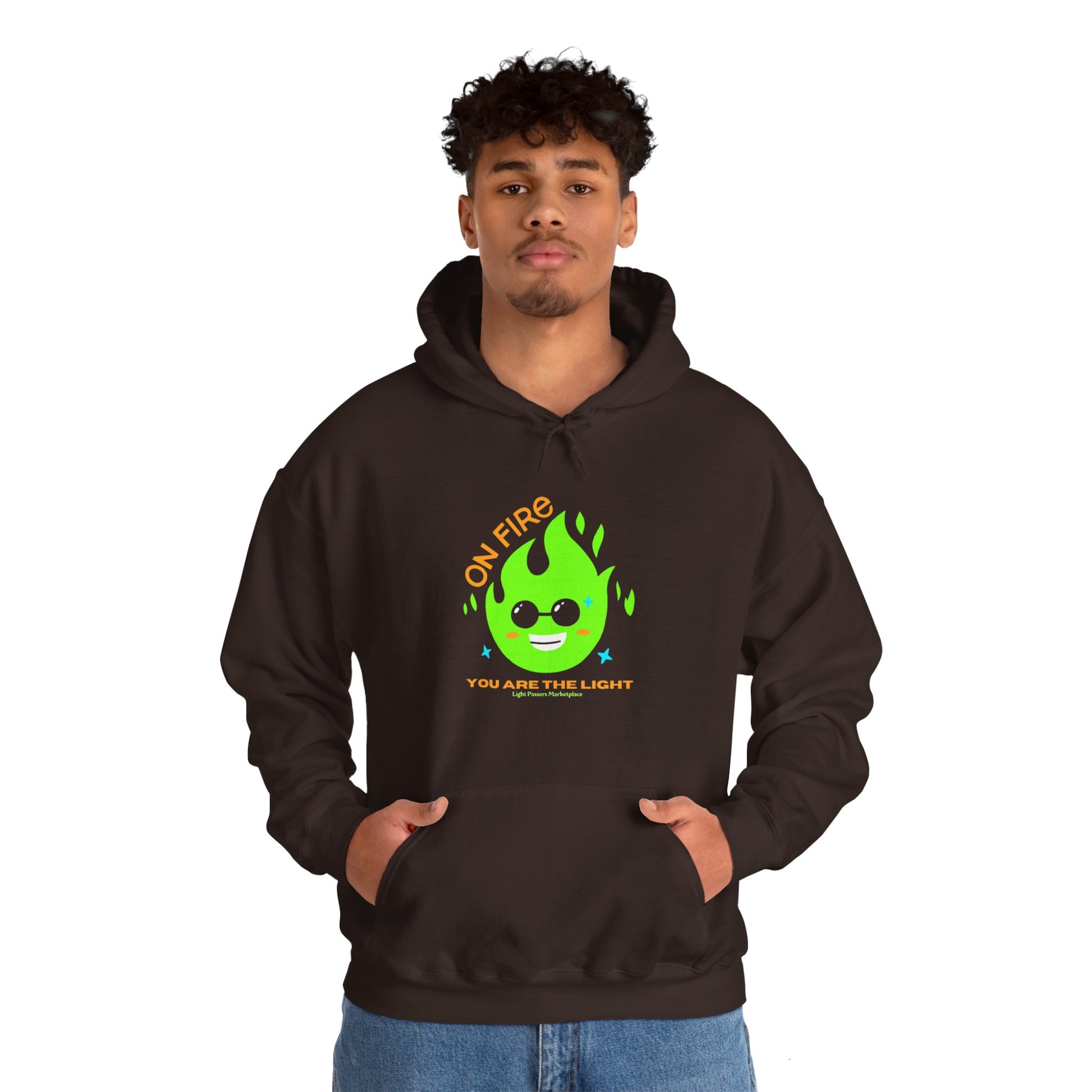 A man in a black hoodie with a green flame design, hands in pockets, showcasing the On Fire You are the Light Unisex Hooded Sweatshirt's cozy blend of cotton and polyester.