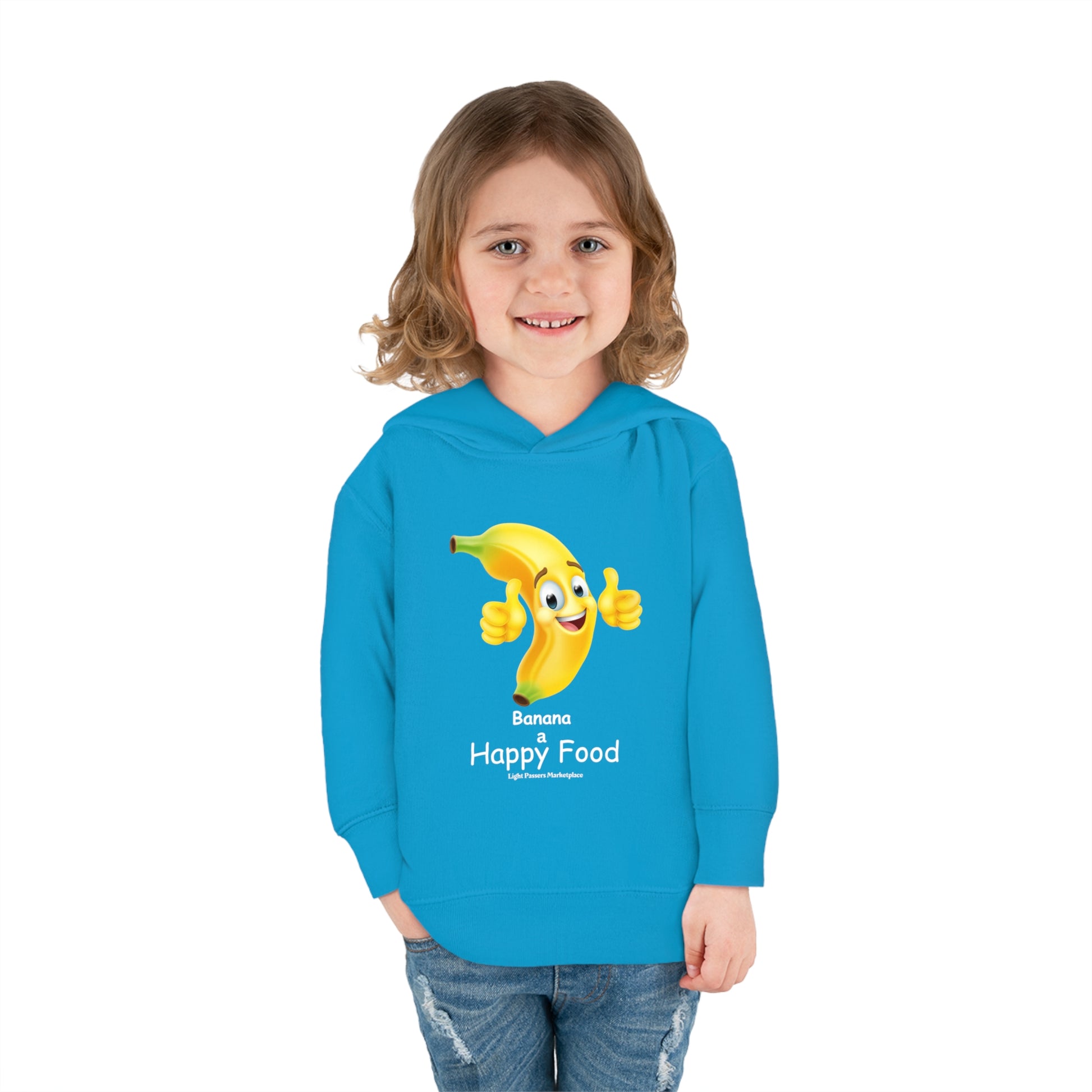 A child in a Rabbit Skins Banana Happy Food Toddler Hooded Sweatshirt, featuring a cartoon banana design, smiling at the camera. Jersey-lined hood, side pockets, and durable stitching for cozy wear.