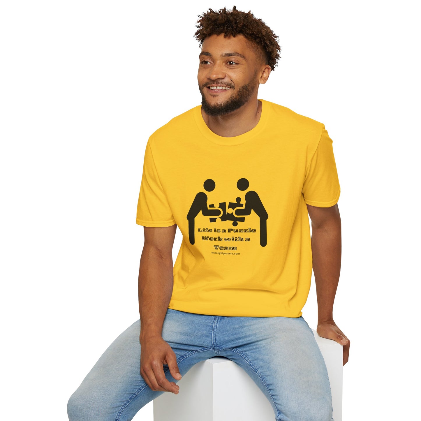 A man in a yellow shirt sits on a cube, showcasing the Life is a Puzzle Team Unisex T-shirt. The image captures a casual, comfortable tee ideal for everyday wear.