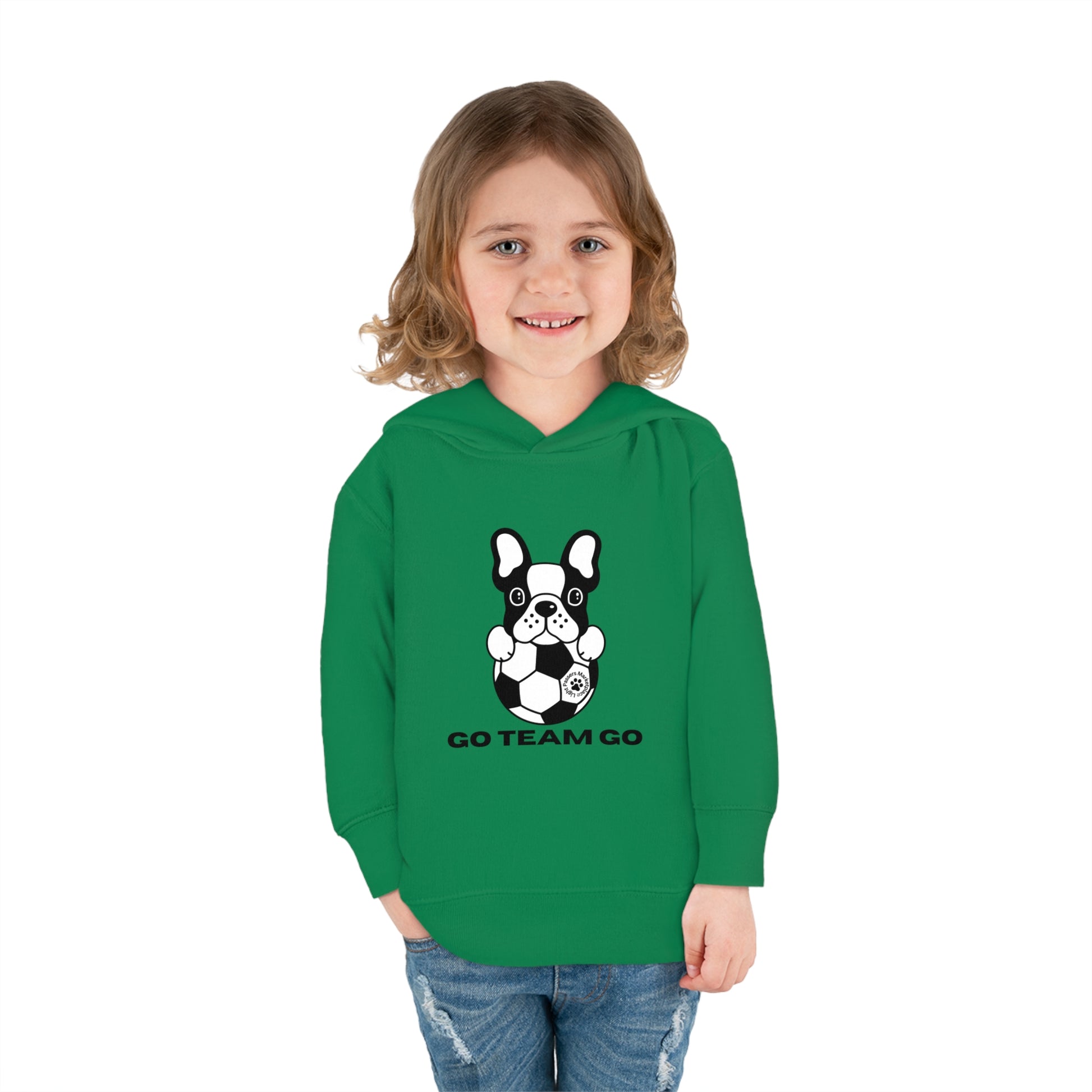 A toddler in a green sweatshirt with a dog design, smiling, featuring cover-stitched details, side seam pockets, and a jersey-lined hood for comfort and durability.