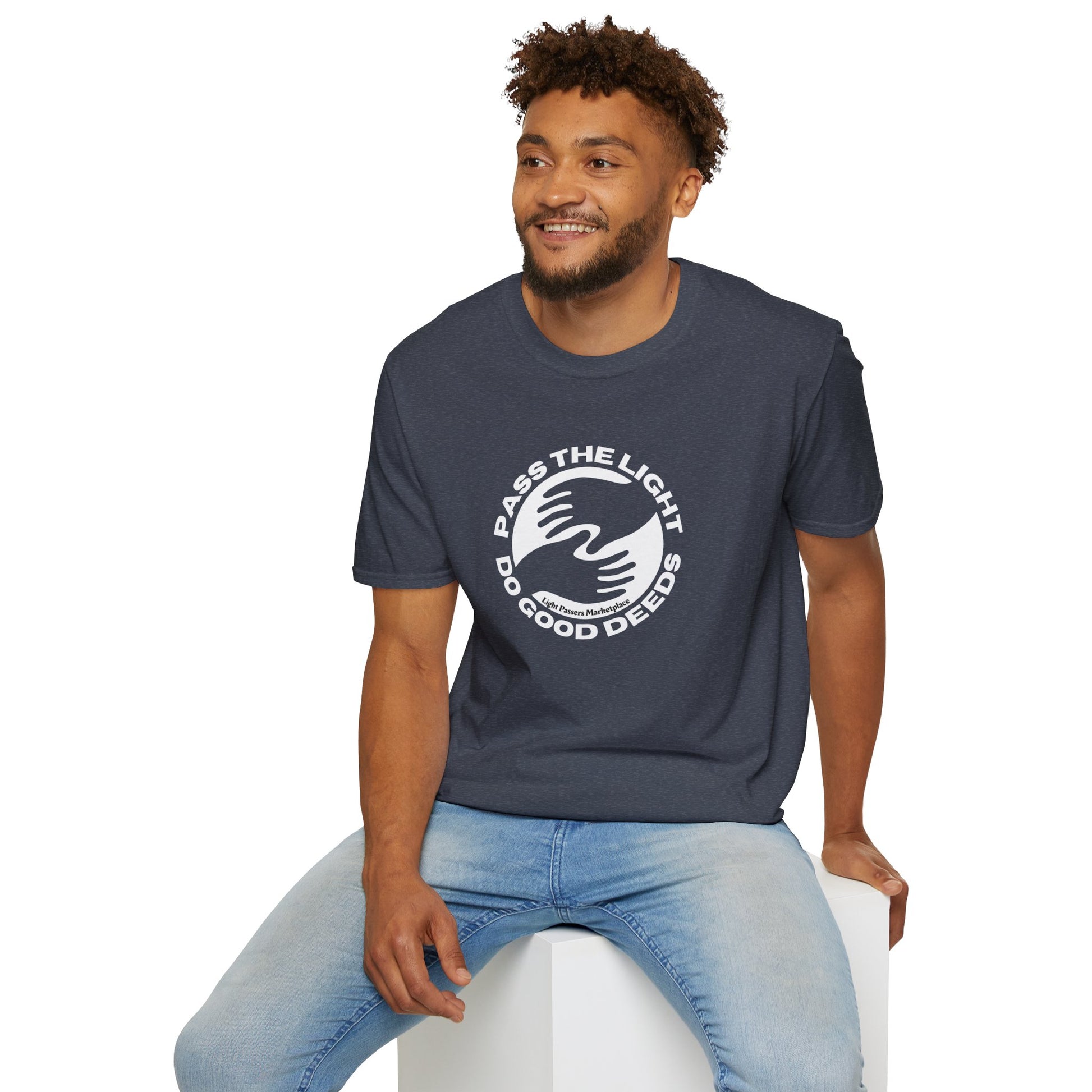 A man in Pass the Light Do Good Deeds Unisex T-shirt sits on a white cube, showcasing the classic fit tee. No side seams, smooth cotton fabric for vibrant prints, and shoulder tape for durability.