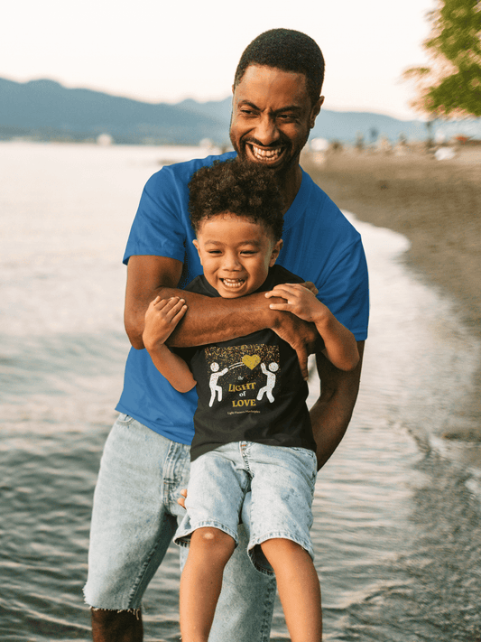 A man holding a child in his arms, wearing a Gold Heart Pass the Light of Love Youth T-shirt. 100% cotton tee with twill tape shoulders, ribbed collar, and no side seams. Classic fit, midweight fabric.