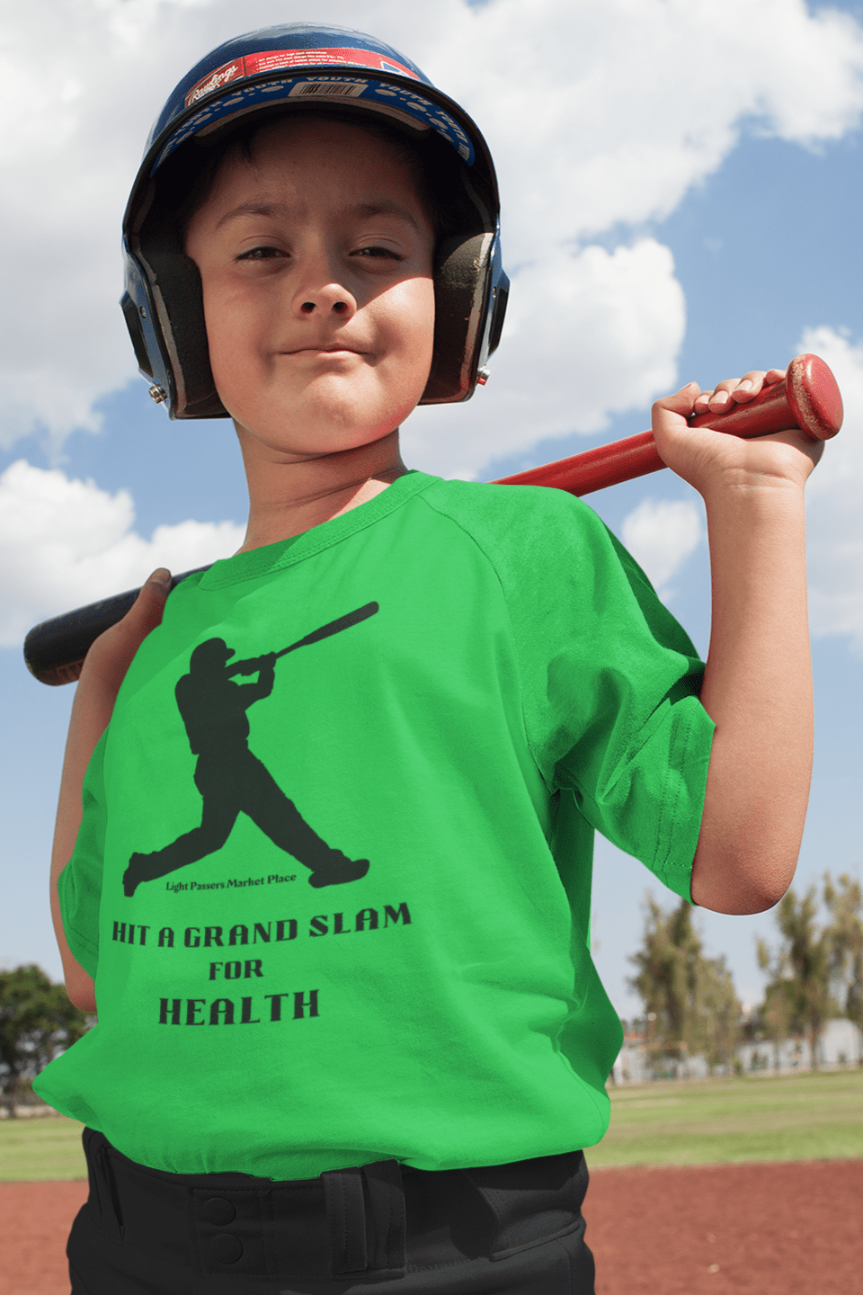 A boy in a green shirt and helmet holds a baseball bat, showcasing the Grand Slam for Health Youth T-shirt. Made of 100% cotton, with twill tape shoulders and ribbed collar for durability.