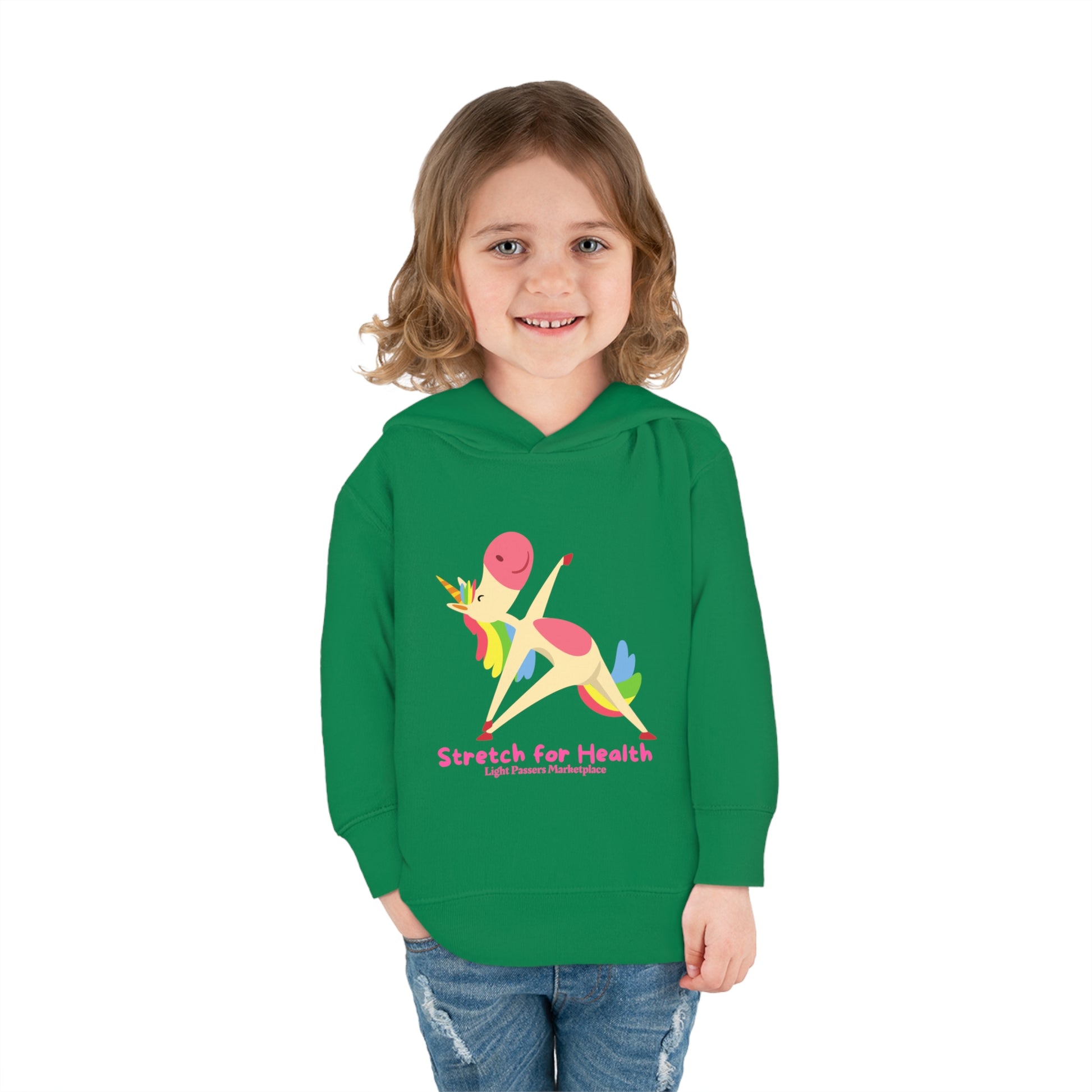 A smiling girl in a Unicorn Stretch Toddler Hooded Sweatshirt with a cartoon unicorn design, showcasing jersey-lined hood and side seam pockets for durable comfort.